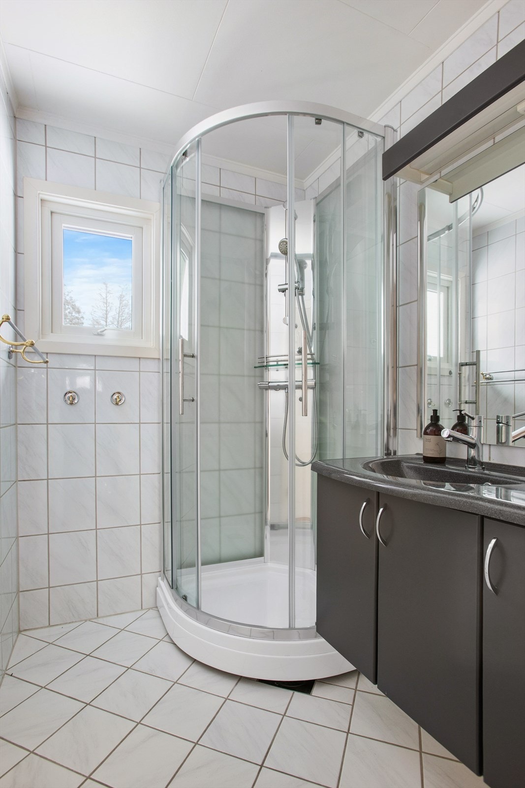 Pent flislagt bad med gulvvarme. Innredet med dusjkabinett og servantskap med speil og belysning Galleribilde