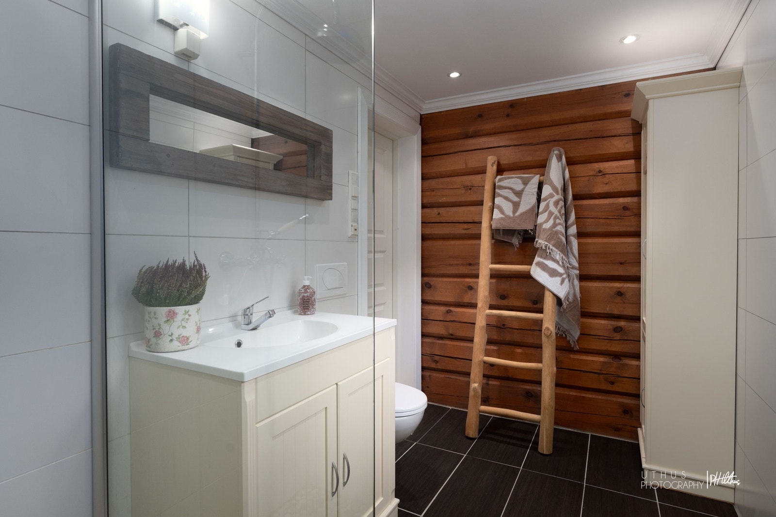 Innslag av tømmervegg mot lyse fliser på badet. Galleribilde