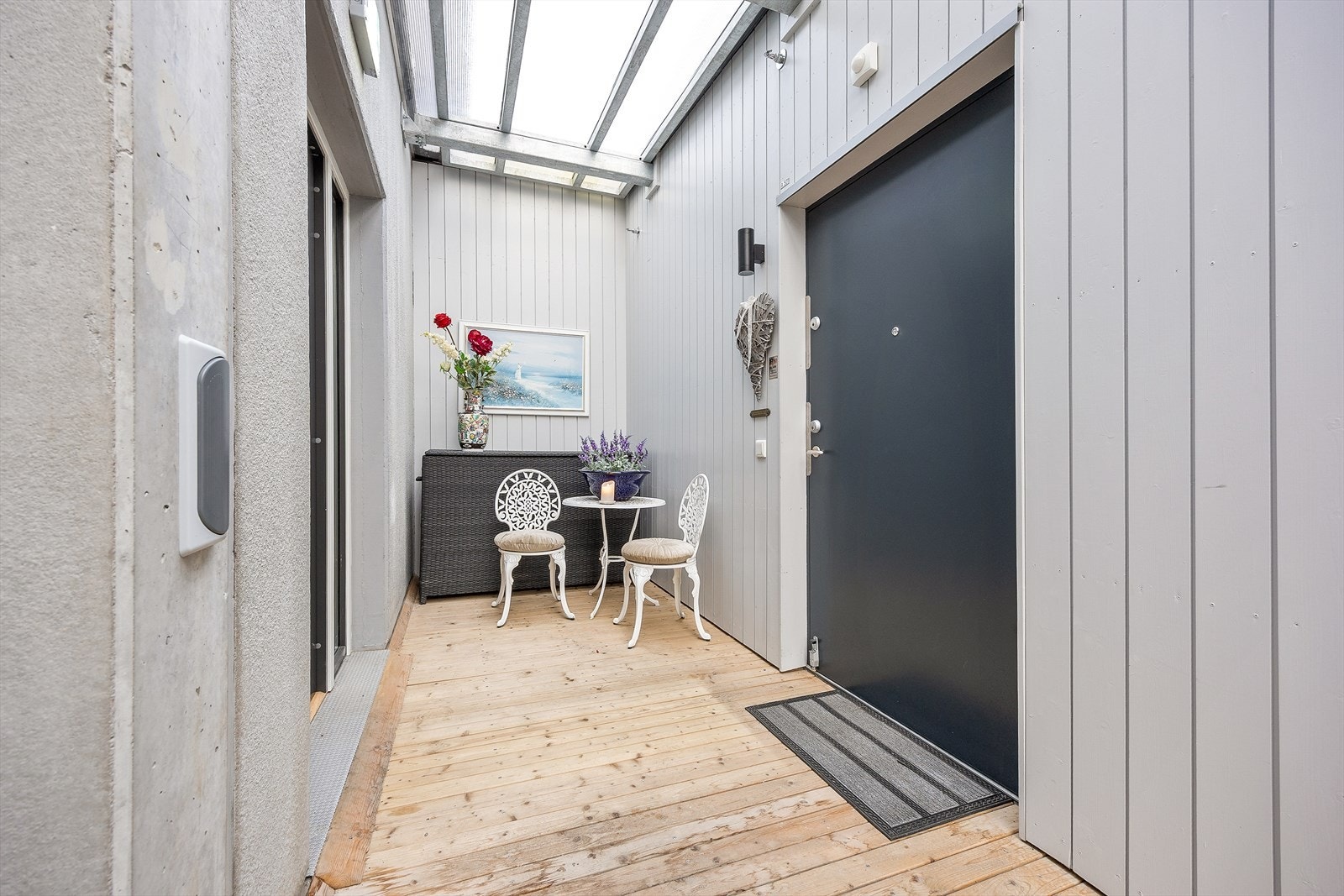Overbygget inngangsparti til leiligheten med plass til kafésett. Her kommer du deg tørrskodd fra garasjen via heisen og til leiligheten. Galleribilde