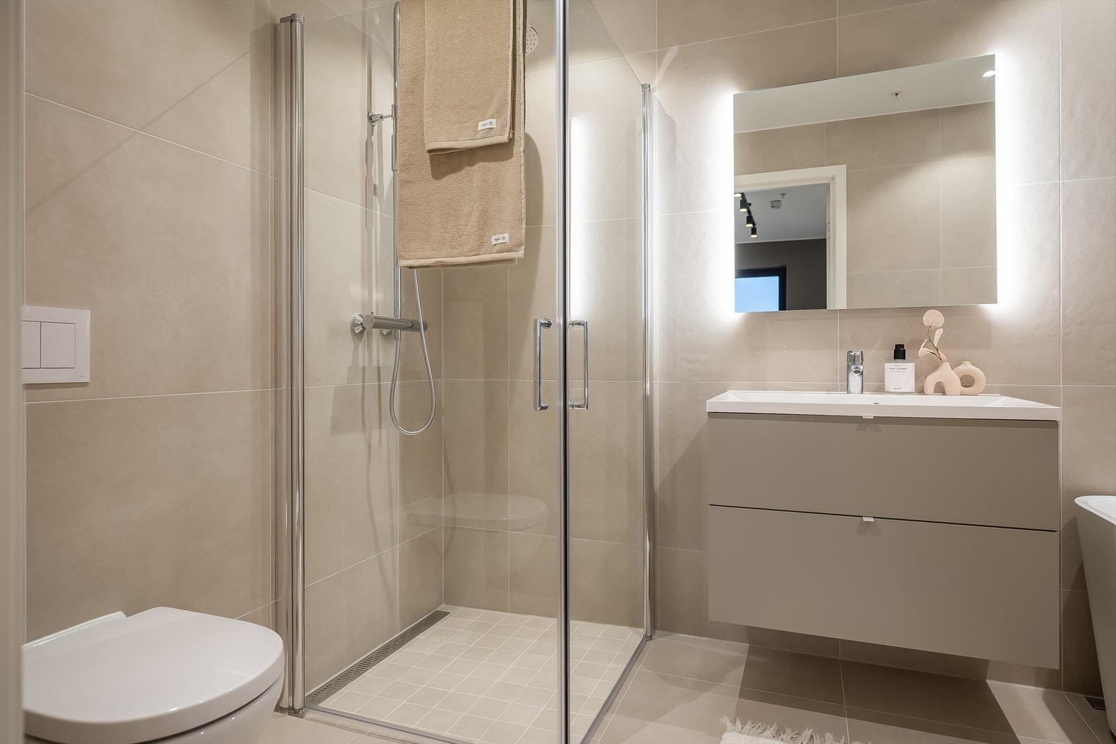 Badet er utstyrt med servant, servantskap, badekar, innfellbare dusjdører og veggmontert wc. Galleribilde