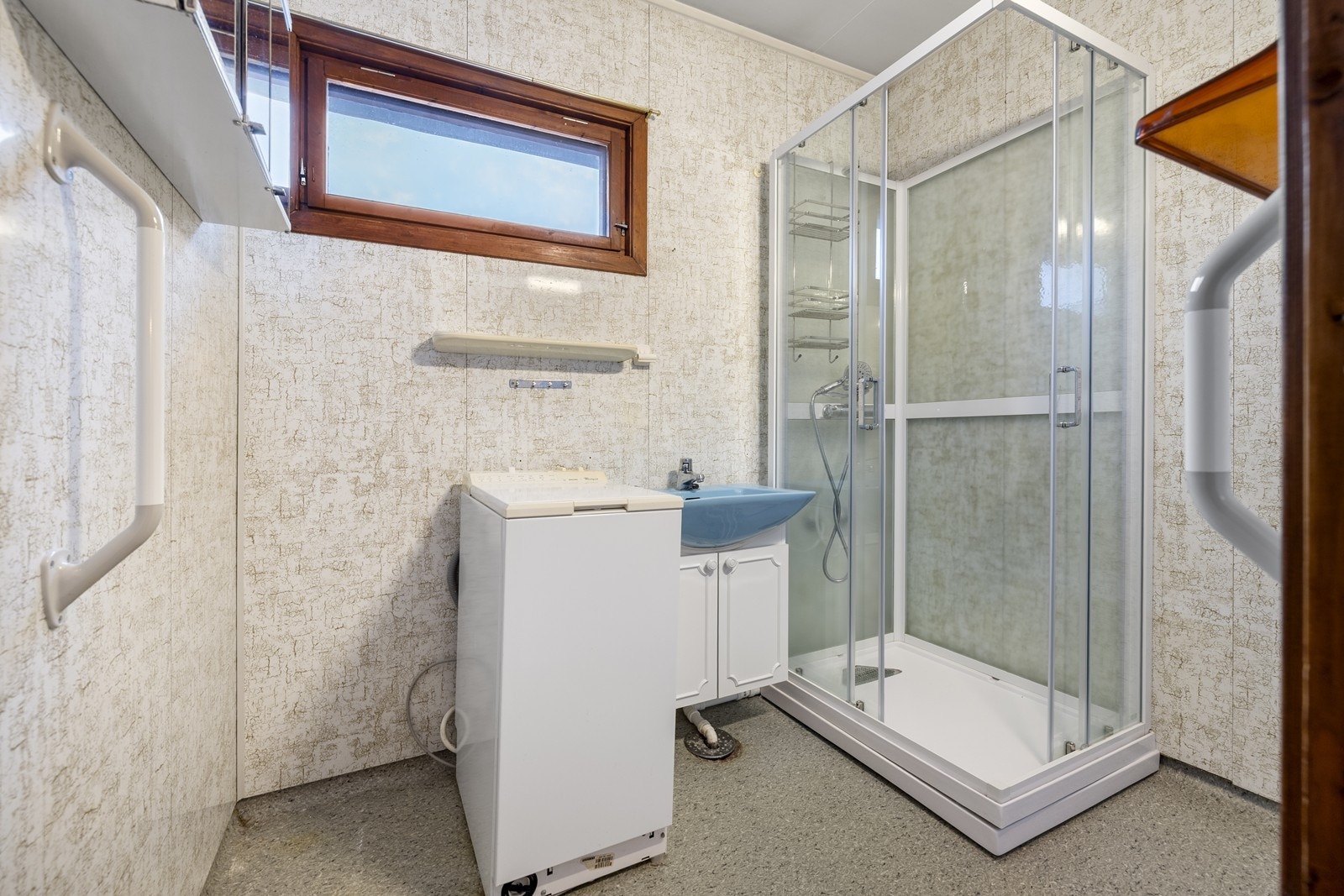Baderom med belegg på gulv og våtromsplater på vegg. Badet består av dusjkabinett, servant og opplegg for vaskemaskin. Galleribilde