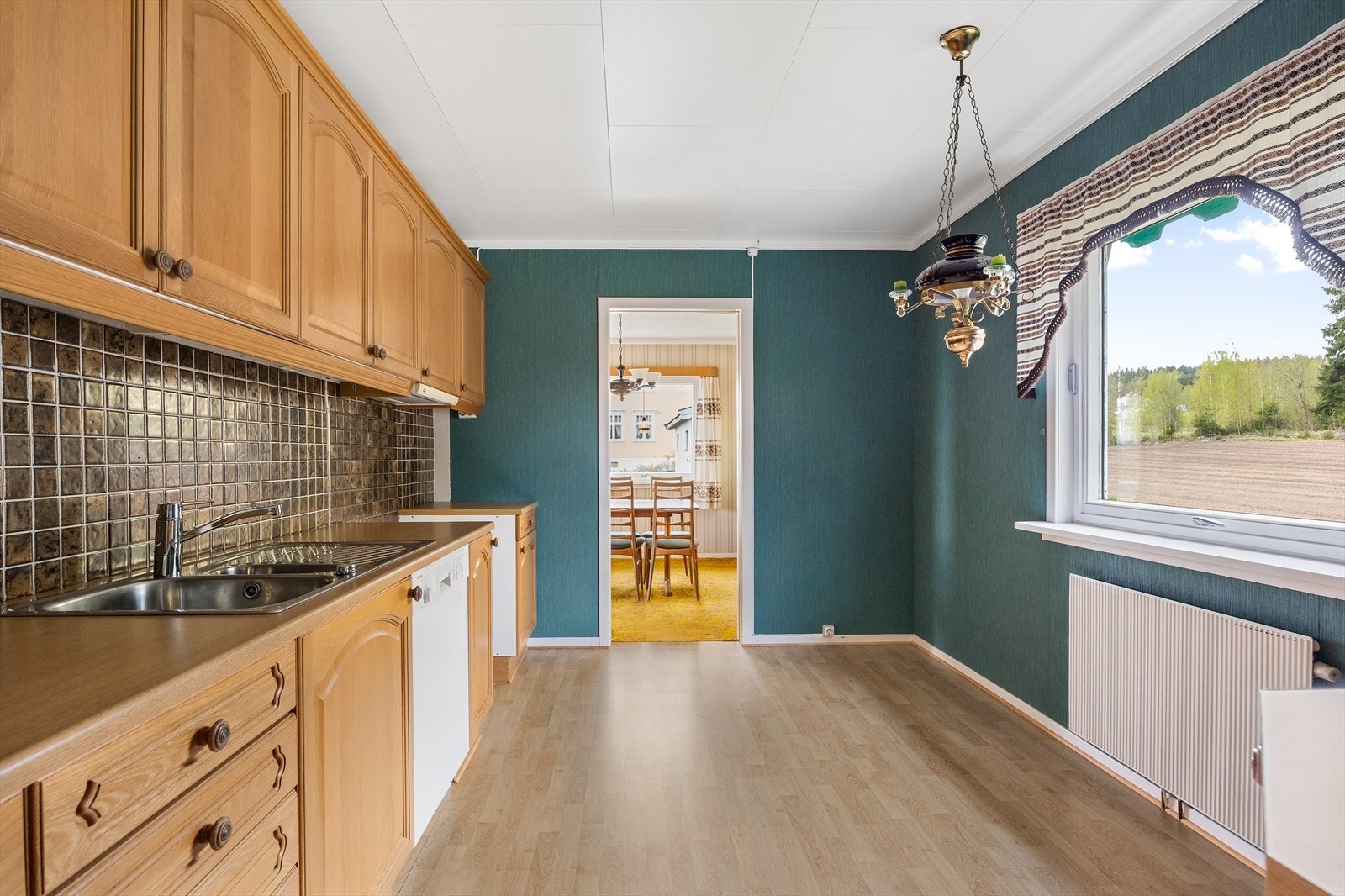 Innredningen har trehvite, profilerte fronter og matchende laminatbenkeplate med vaskekum i stål.
Det er nisje for komfyr, plass til kjøleskap og opplegg for oppvaskmaskin. Galleribilde