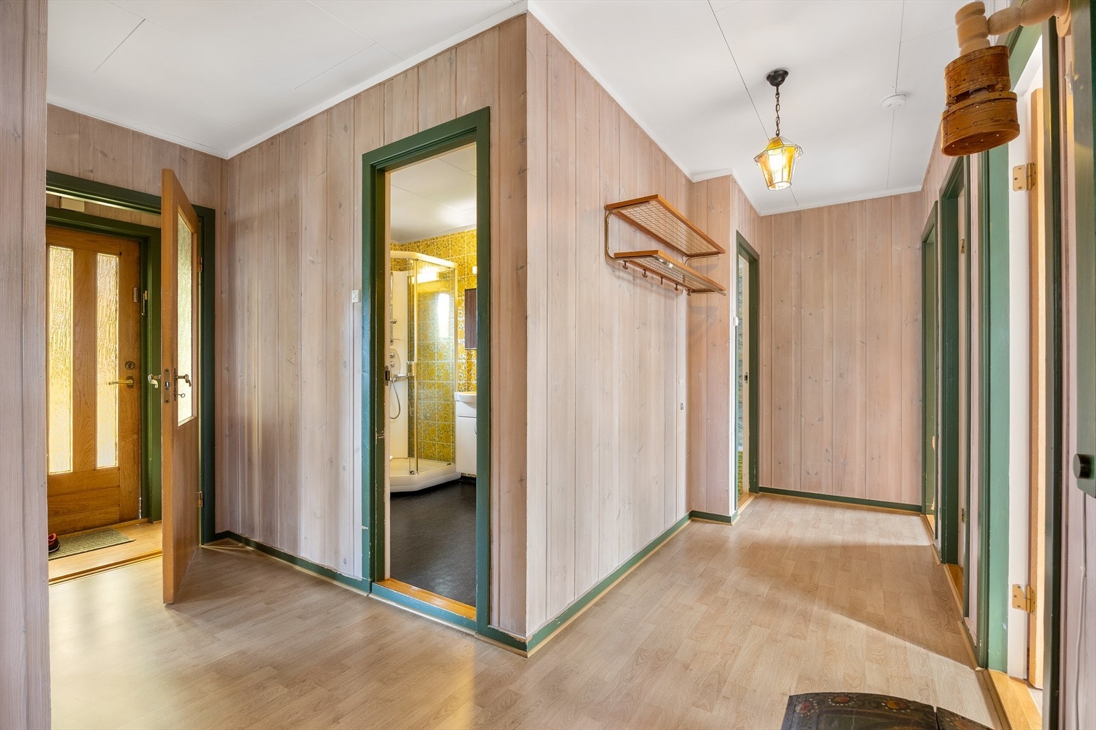 Vindfanget har lyst laminatgulv og panelvegger. En dør med glassfelt fører inn til en større gang med plass til oppbevaringsmøblement. Galleribilde