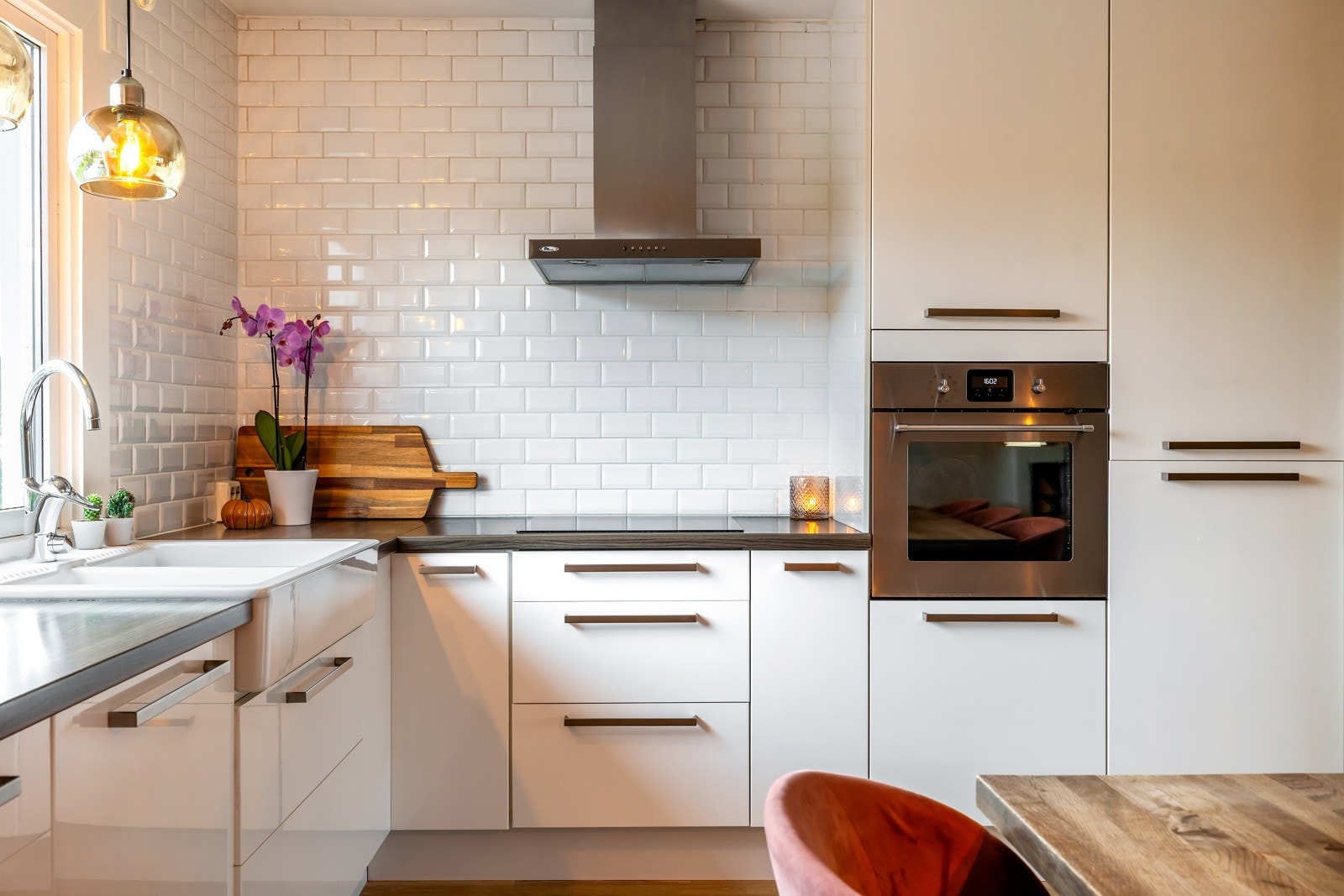 De hvite, høyglansede frontene gir et moderne uttrykk, kombinert med mørk laminatbenkeplate og klassiske fliser over benken. Galleribilde