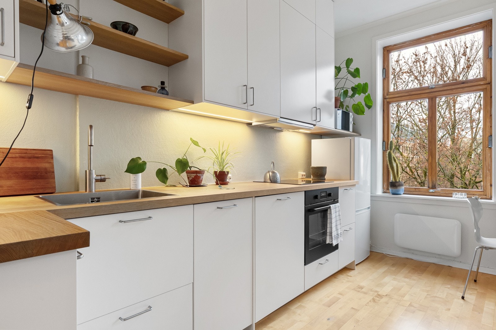 Plassbygde eikehyller gir ekstra oppbevaringsmuligheter. Under overskapene er det dimbar belysning og stikkontakter. Galleribilde