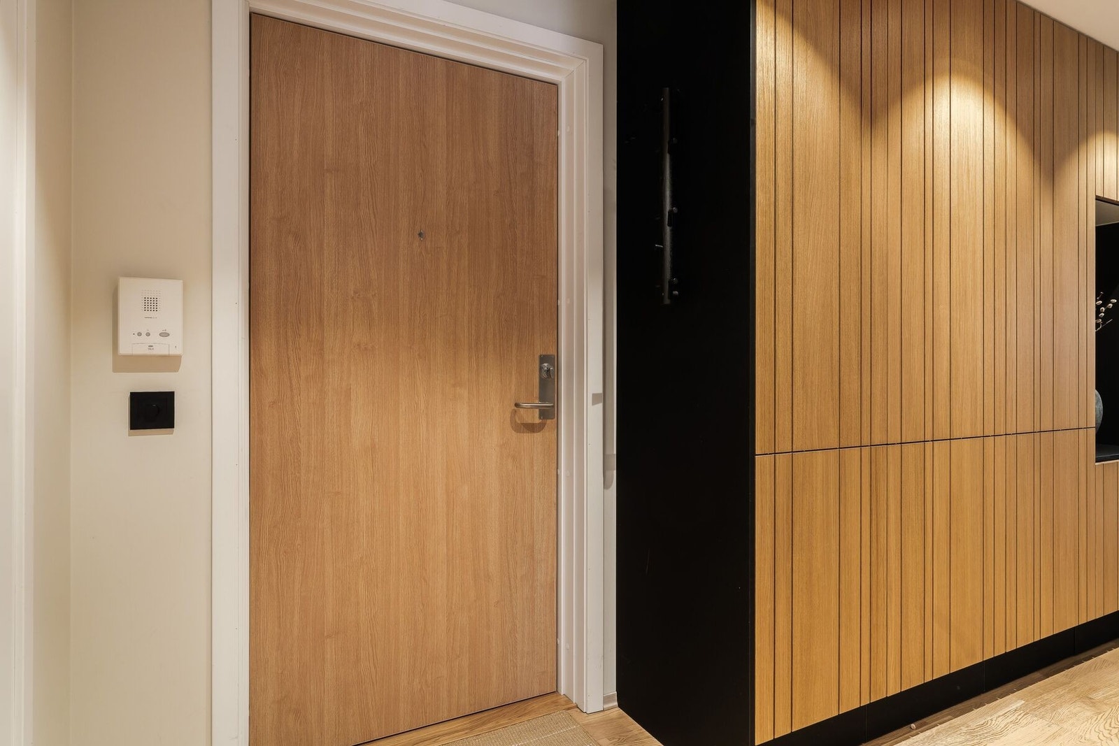 Allerede idet du trer inn i boligen, møter du en rolig og gjennomført helhet. Gangen er elegant innredet med spesialbestilte garderobeskap fra JKE, tilpasset kjøkkenets design og materialvalg. Galleribilde