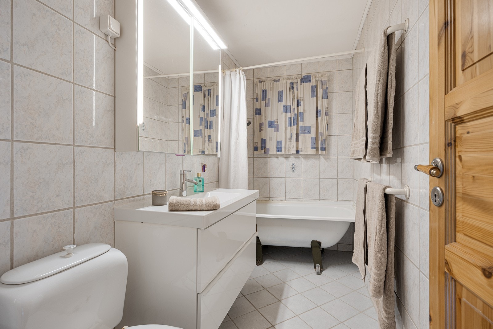 Det helflisede badet har heldekkende servant over hvite høyglansfronter og dobbelt speilskap med integrert belysning over.
Videre har badet toalett, badekar med dusjarmatur og lun gulvvarme. Galleribilde