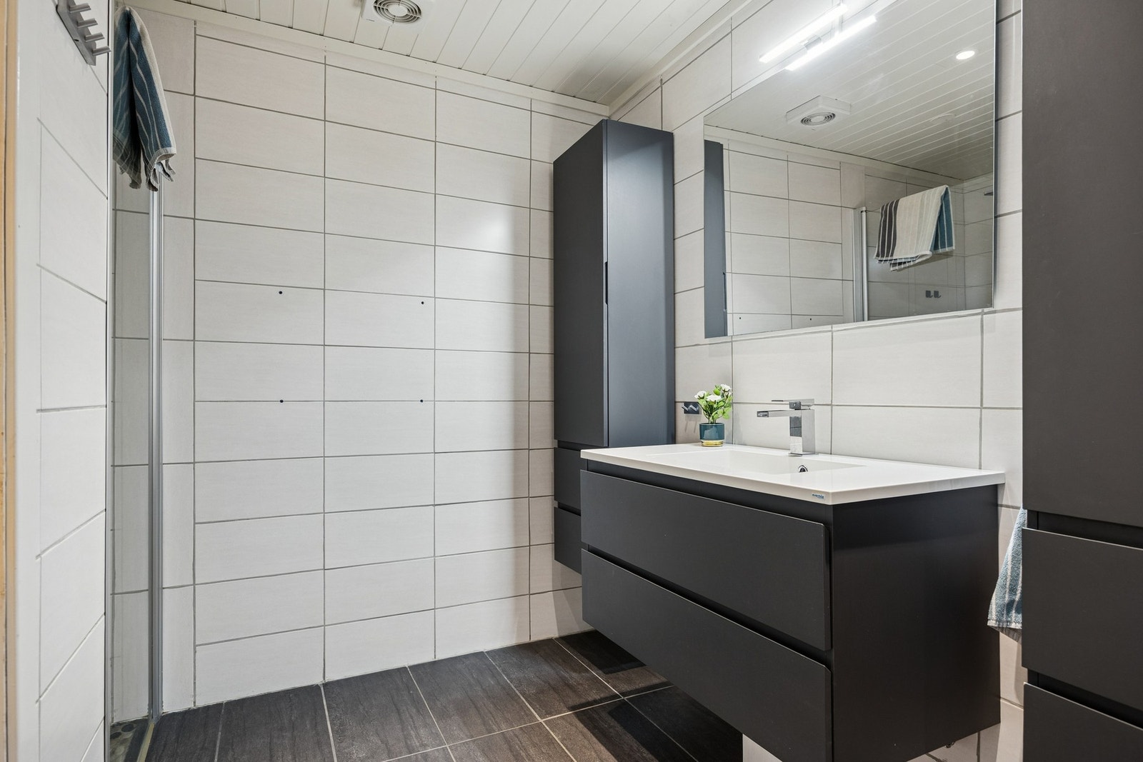 Badet er utstyrt med vegghengt servantinnredning, speil med overlys, vegghengte høyskap, dusjhjørne med dører og vegghengt toalett. Galleribilde