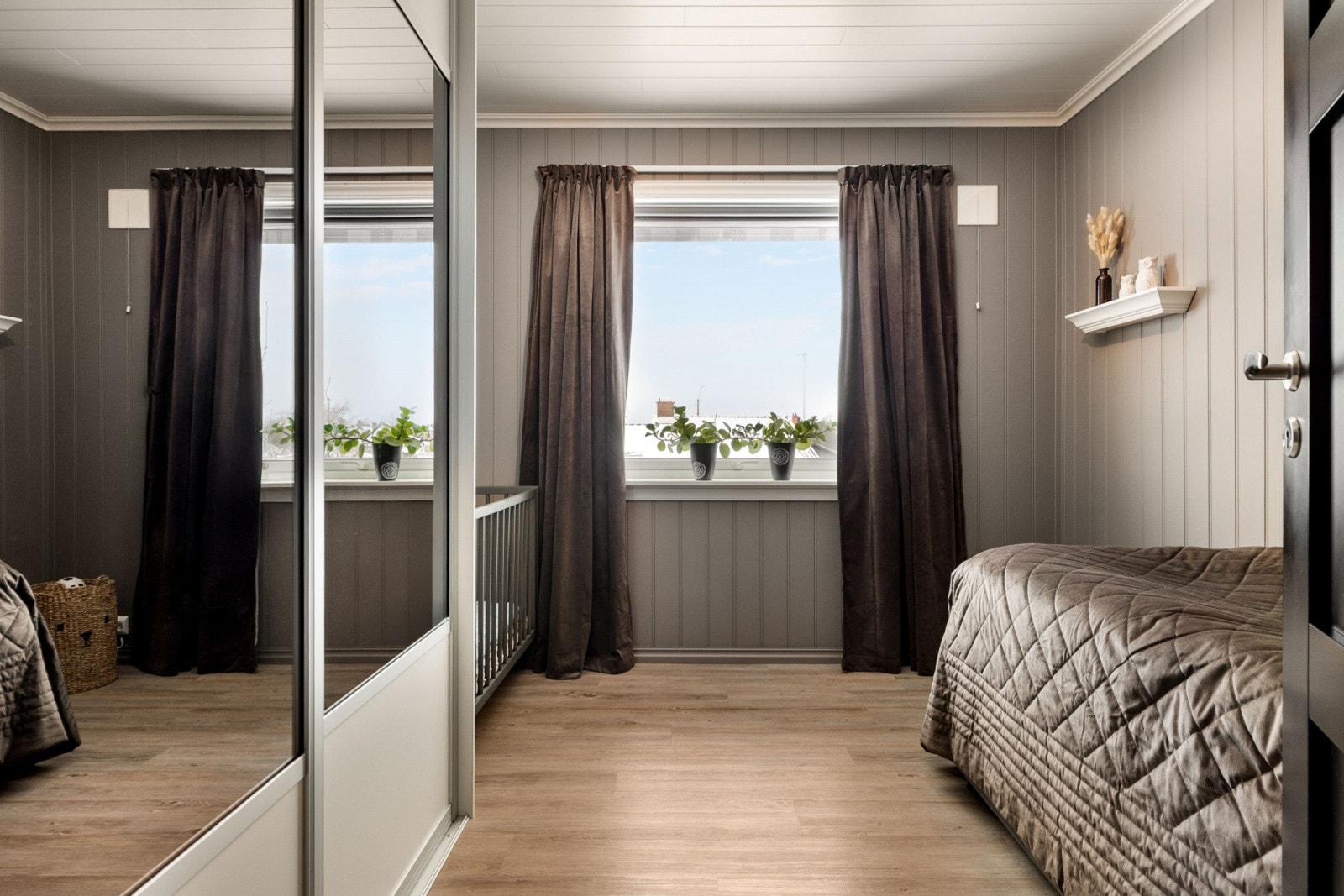 Rommet har grå vegger, lyst tak, laminatgulv og vindu med utsikt over nabolaget. Garderobeskap med speildører gir ekstra romfølelse. Galleribilde