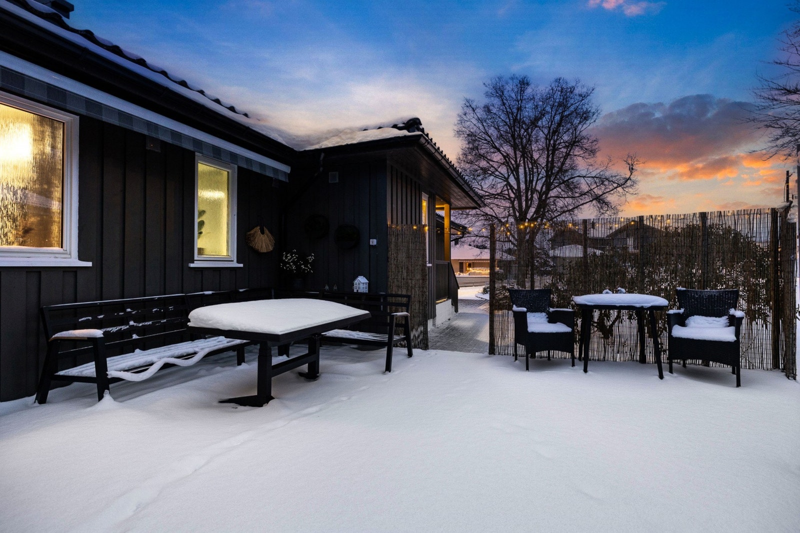 Uteområde med snødekt terrasse og koselig belysning. En flott uteplass hele året, men ekstra lunt og hyggelig på sommerstid. Galleribilde