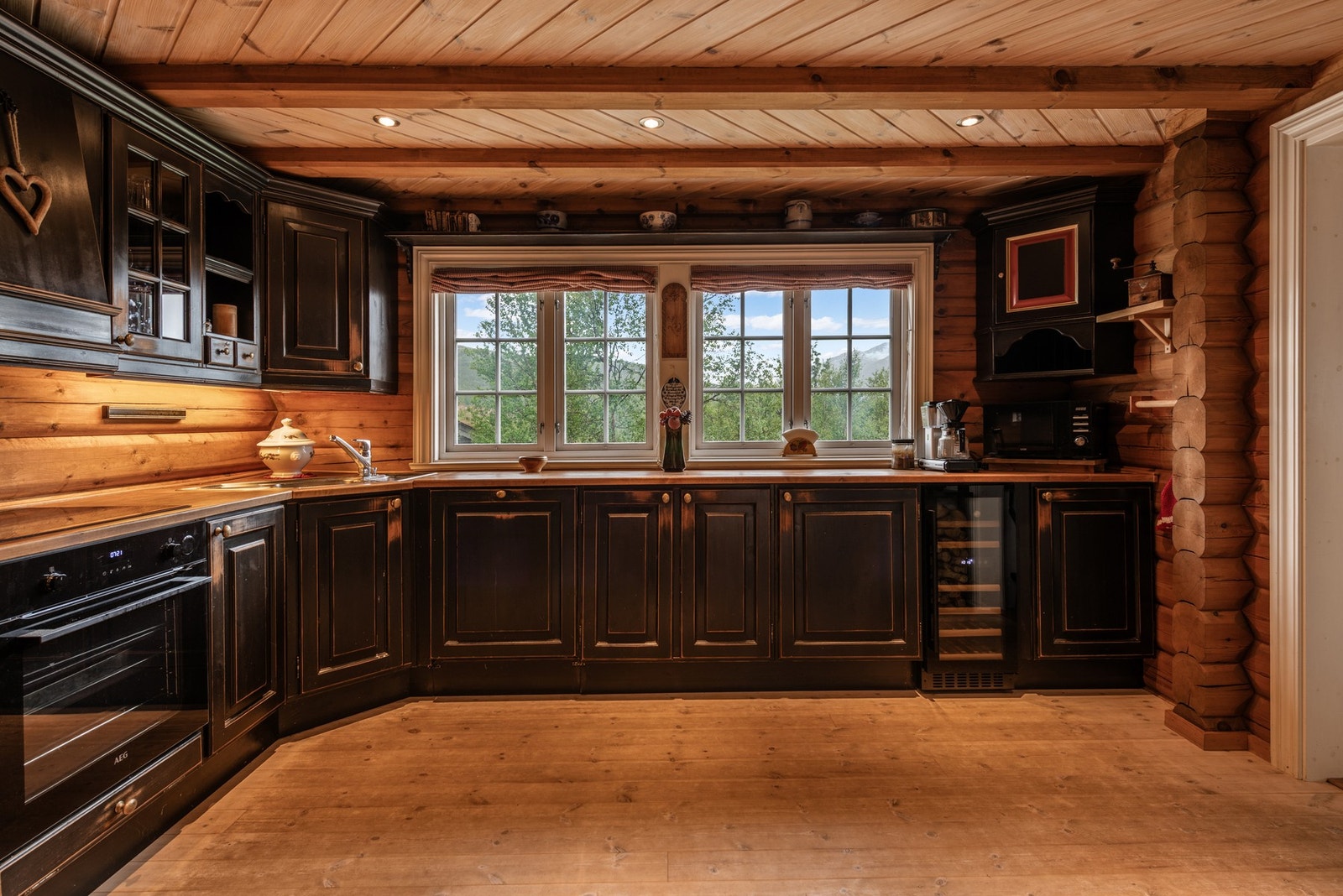 Velutstyrt kjøkken med heltre innredning og benkeplater. Inneholder oppvaskbenk, overskap, kjøkkenventilator med avtrekk ut, og integrerte hvitevarer Galleribilde