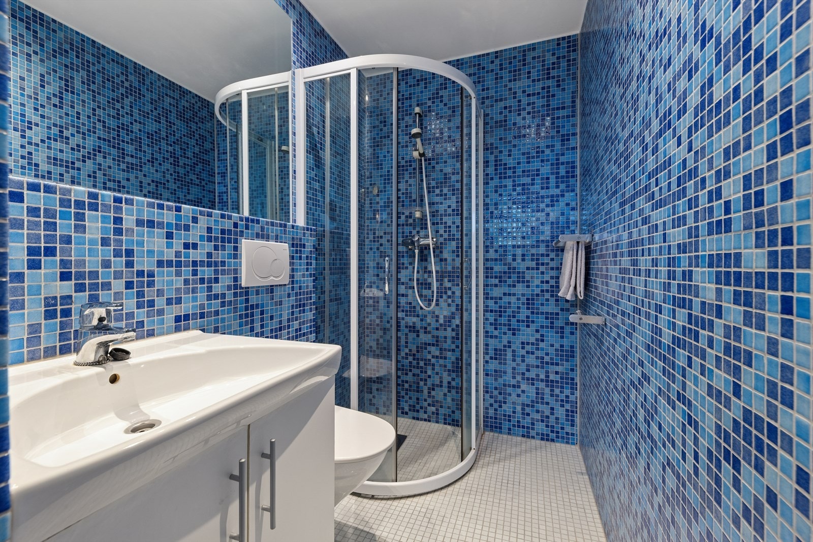 Flislagt baderom innredet med servant med underskap, dusj og vegghengt toalett. Det er varmekabler i gulvet som gir behagelig gulvvarme - en praktisk og komfortabel løsning for hybelen. Galleribilde