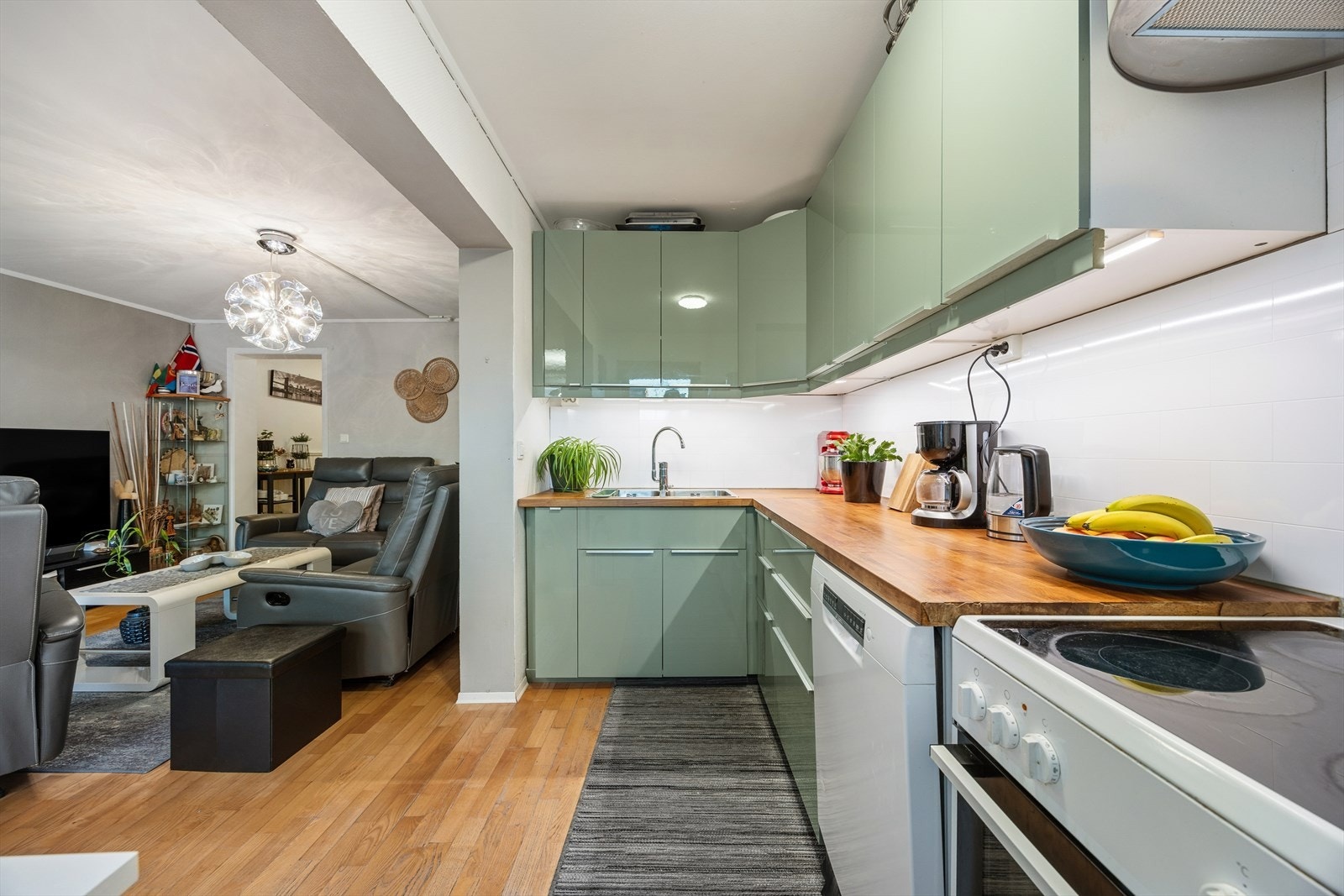 Frittstående hvitevarer med oppvaskmaskin, komfyr og kjøl/frys. Stikkontakt på vegg over benk, laminat mellom benk og overskap samt lys under overskap. Galleribilde