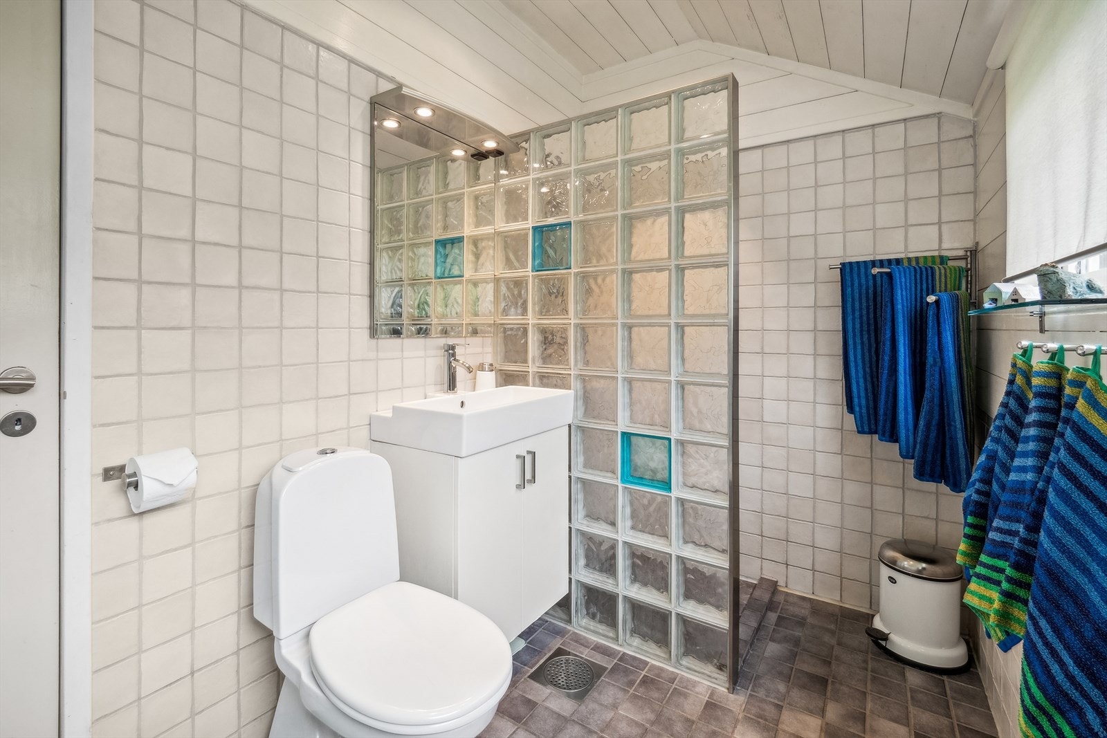 Badet har fliser og panel på veggene samt fliser på gulvet med gulvvarme. Innredet med servant med skapseksjon, toalett og dusjhjørne, samt naturlig ventilering. Galleribilde