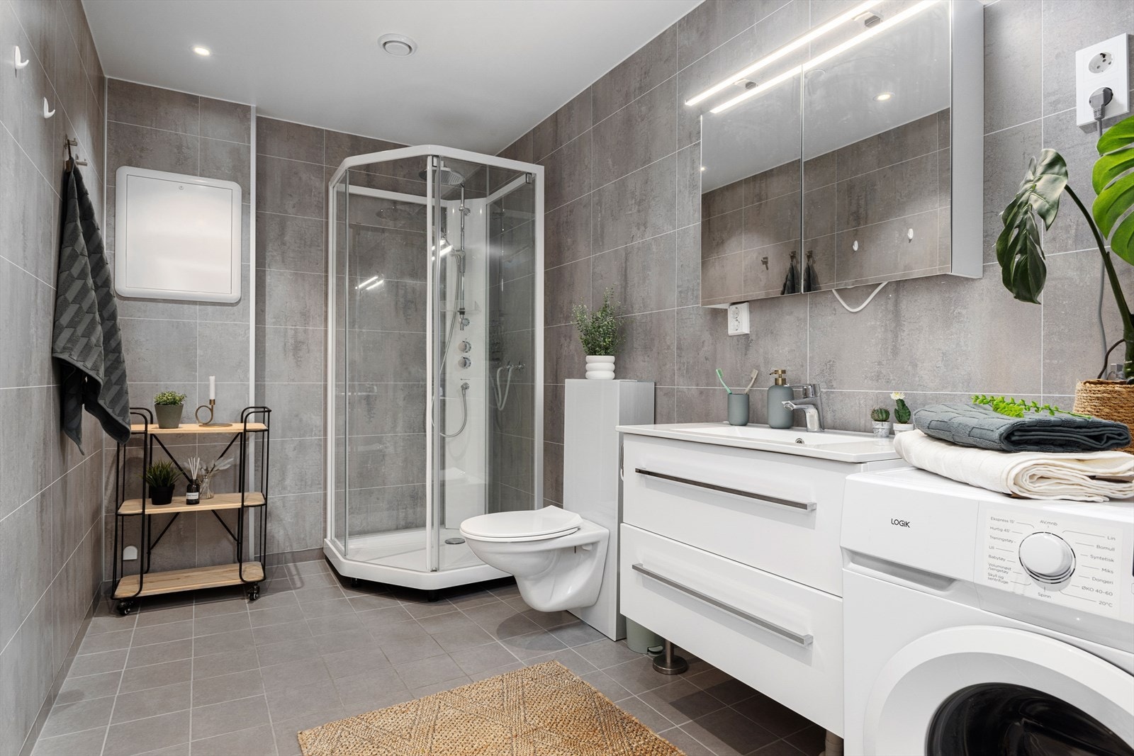 Badet er stort, med flislagt gulv og våtromsplater på vegger. Opplegg for vaskemaskin og varmekabler i gulv. Galleribilde