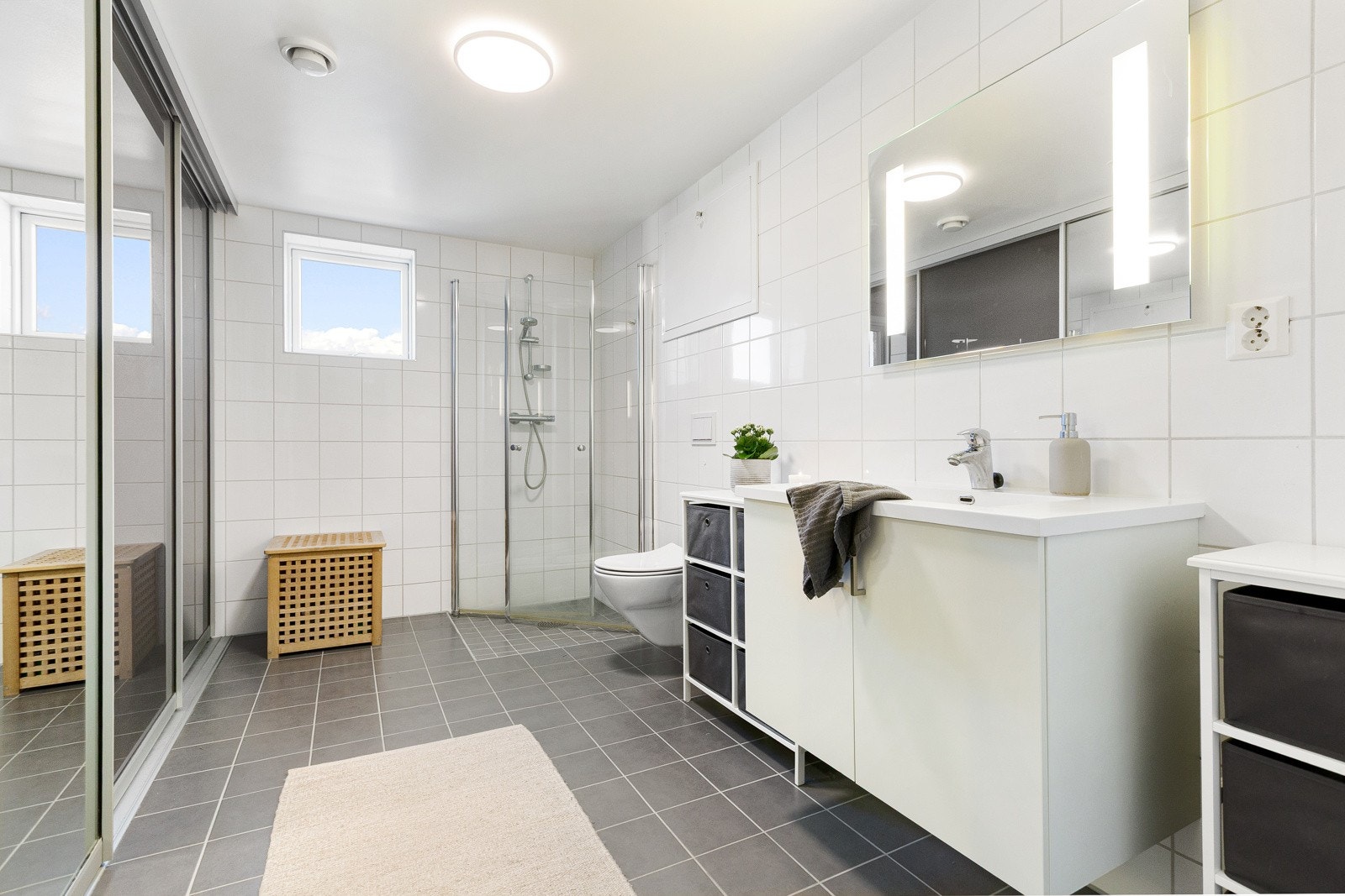 Flislagt bad med dusj, servant og wc. Her er det kjekk skyvedørsgarderobe med speil som skjuler vaskemaskin. Galleribilde