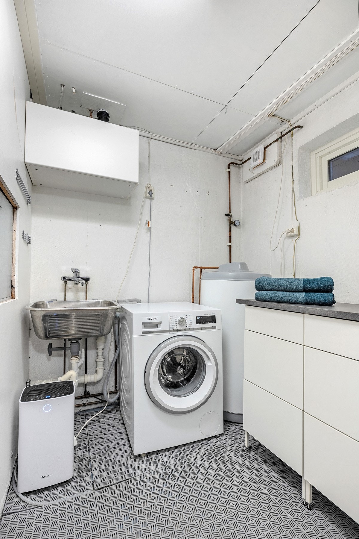 Vaskerom med plass til vaskemaskin, utslagskum og varmtvannsbereder. Praktisk løsning for klesvask og oppbevaring. Galleribilde