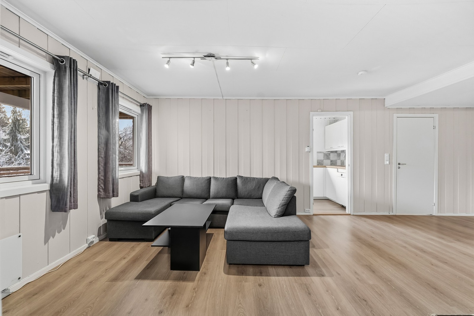 Lys og åpen stue med med lysmalt panel på veggflater og laminat på gulv. Store vindusflater slipper inn godt med lys. Galleribilde