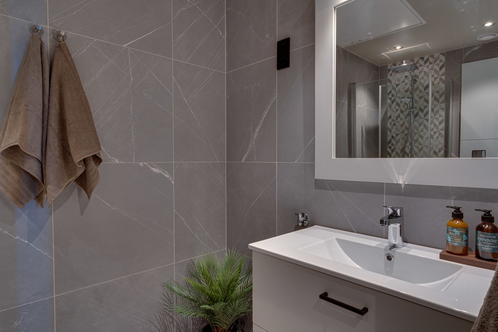 Badet er utstyrt med baderomsinnredning med heldekkende servant og skuffeløsning, samt dusjnisje med glassdører og regnfallsdusj. Videre har badet toalett, downlights, vannbåren gulvvarme og opplegg for vaskemaskin. Galleribilde