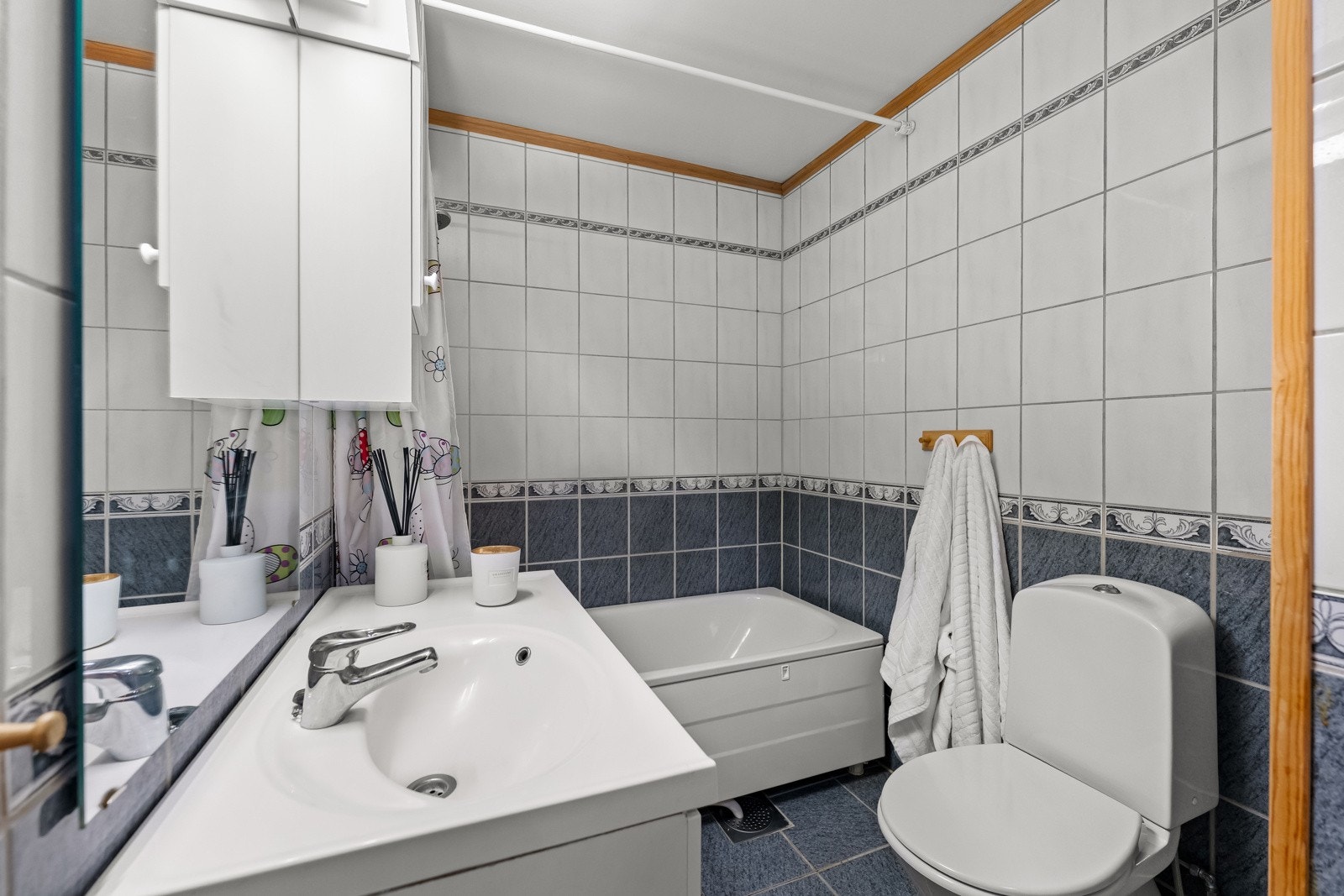 Bad med flislagte overflater som gir et rent uttrykk. Baderomsinnredning bestående av benkeskap og veggskap med profilerte fronter. Videre har badet dusj i badekar, servant og gulvstående klosett. Galleribilde