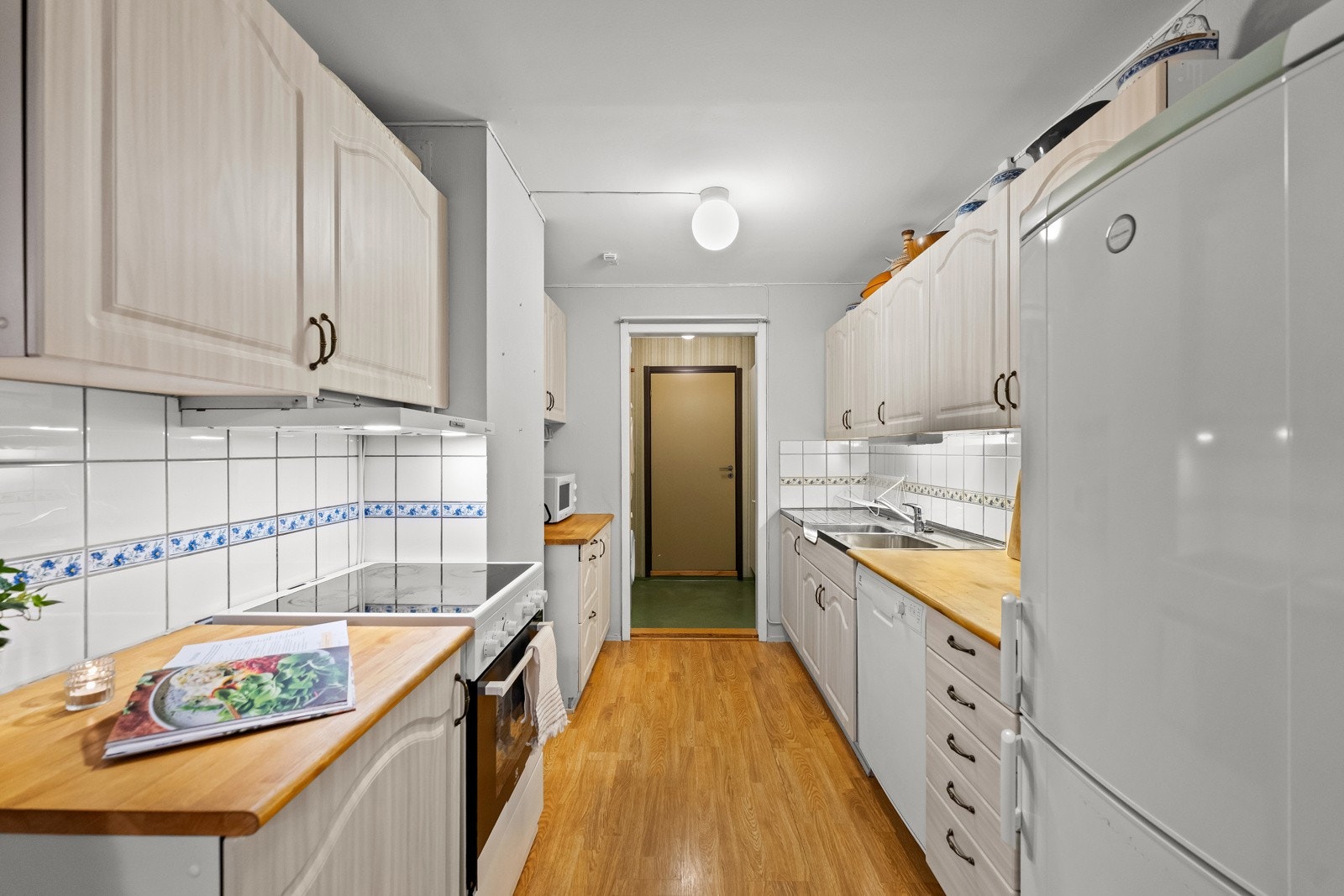 Kjøkkeninnredning med profilerte fronter, benkebeslag i rustfritt stål med utslagskum og kum, heltre benkeplate, ventilator og frittstående hvitevarer. Galleribilde
