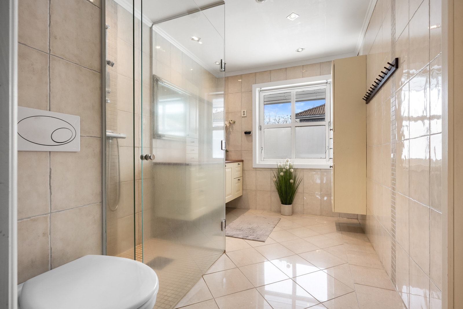 Baderom fra vurdert til å være fra 2005 (datostemplet avløpsrør i sluk). Det er flislagt gulv med varme og flislagte vegger, himling med malt slett flate og downlights, og vegghengt servantskap med profilerte fronter. Galleribilde