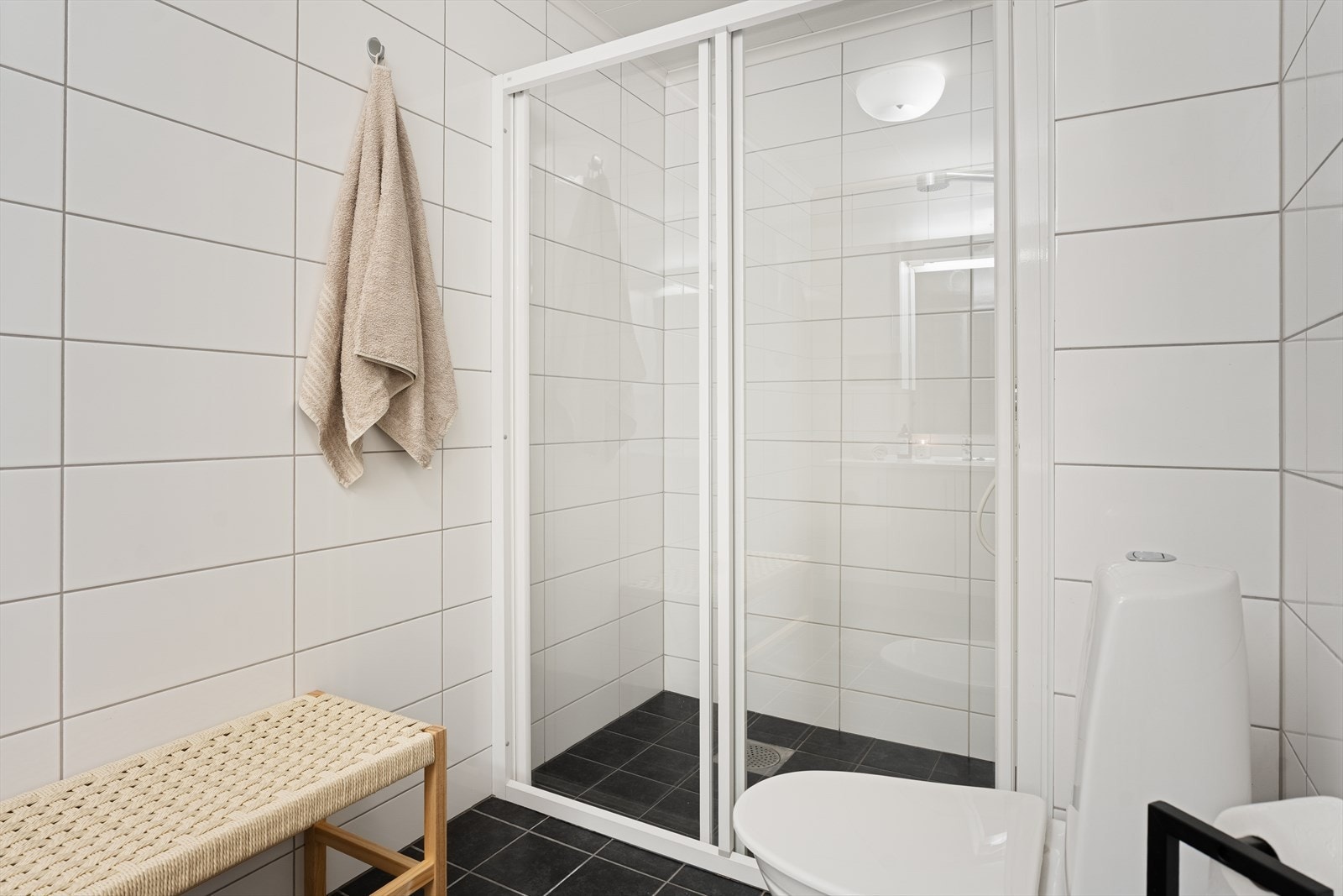 Badet er innredet med hvit baderomsinnredning, gulvstående toalett og romslig dusjnisje med skyvedør i glass og aluminiumsprofile Galleribilde