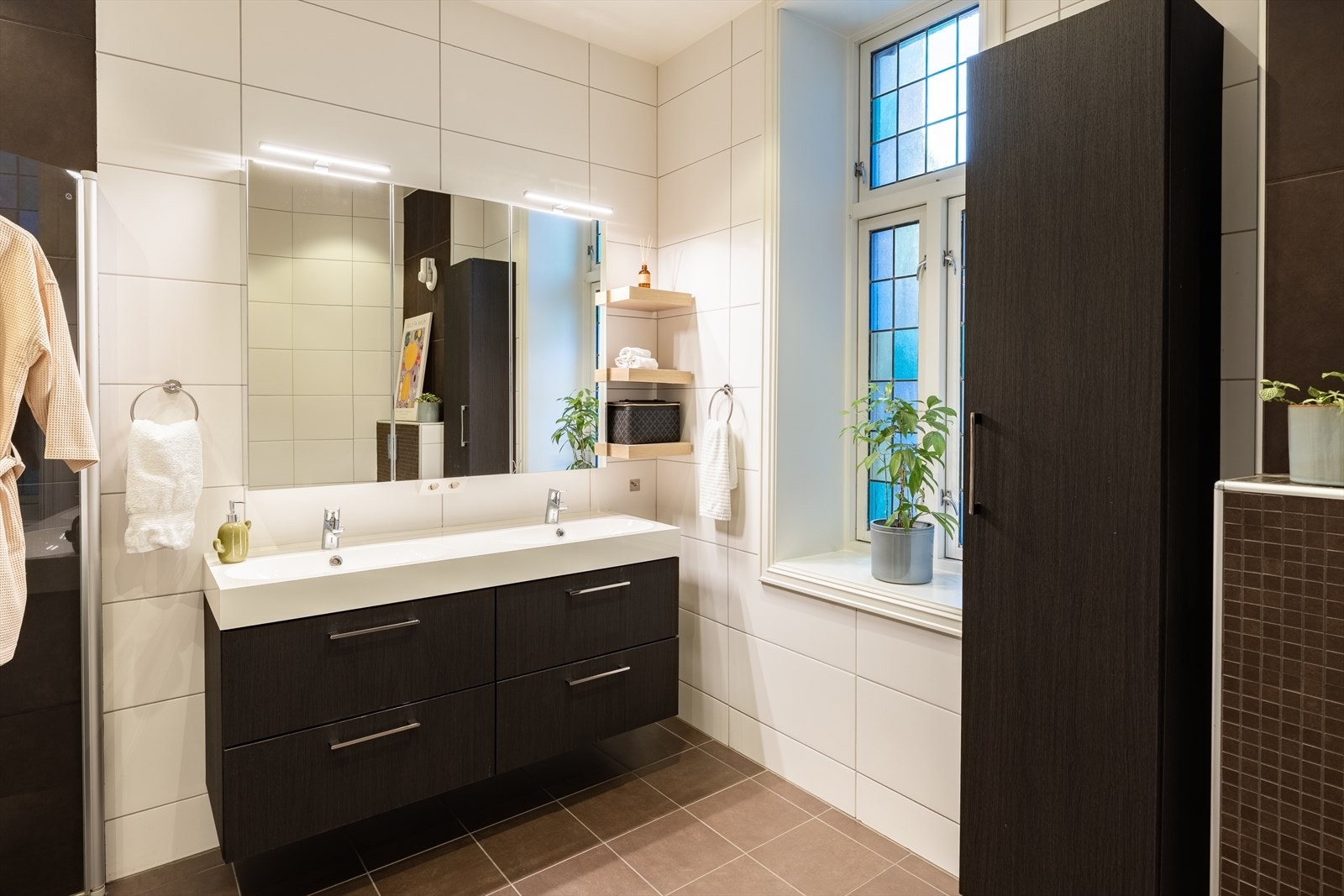 Vegghengt klosett, stort dusjhjørne med innfellbare dusjvegger, moderne innredning med dobbelservant og opplegg for vaskemaskin. Spotter i himling. Galleribilde