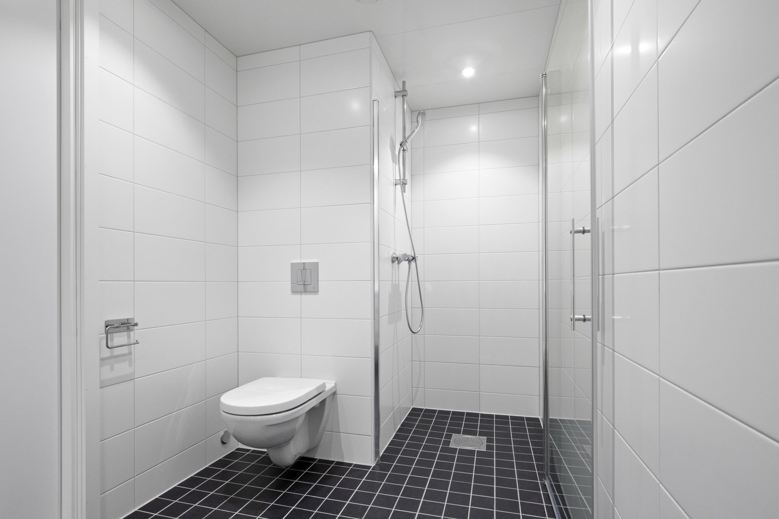 Dagene får en god start på badet, innredet med hvite fliser på veggene og sorte mosaikkfliser på gulvet Galleribilde