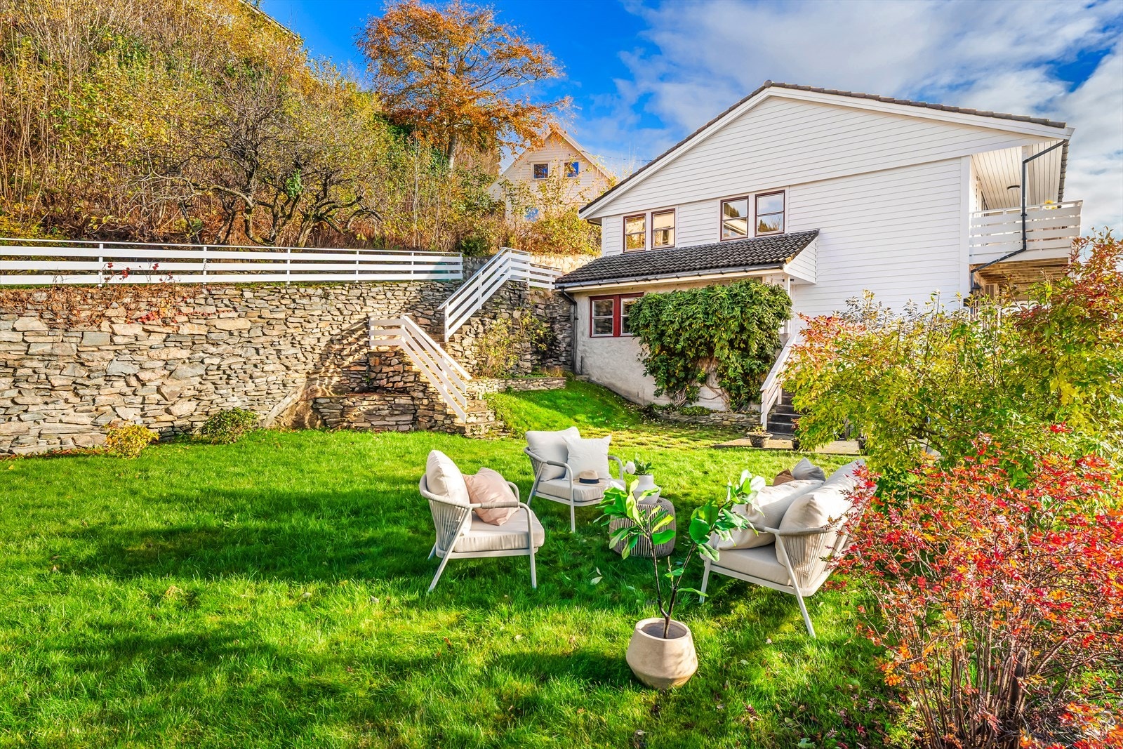 Ute finner man en stor, flat tomt med plen og en velholdt hage med beplantning Galleribilde