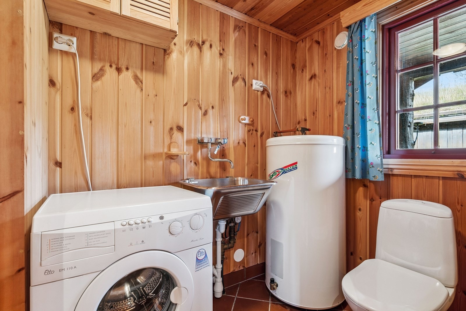 Innenfor entréen ligger et praktisk vaskerom med skyllekum, varmtvannsbereder, opplegg for vaskemaskin, samt toalett. Ett rom som er både funksjonelt og behagelig å bruke. Galleribilde