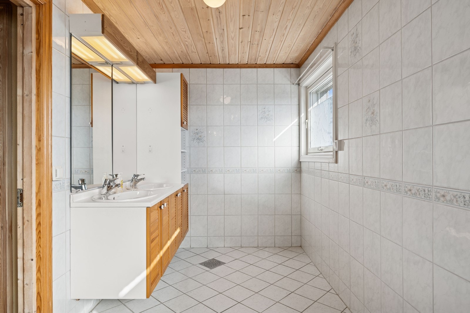 Lyst, flislagt baderom som har innredning med to nedfelte servanter. Varmekabler i gulv. Galleribilde