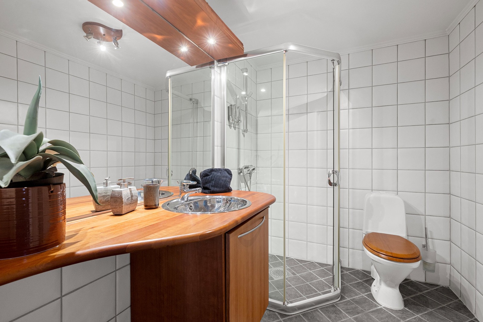 Praktisk baderom med adkomst fra hall, innredet med dusjhjørne, servantinnredning med benkeplate i tre og flislagte overflater. Galleribilde