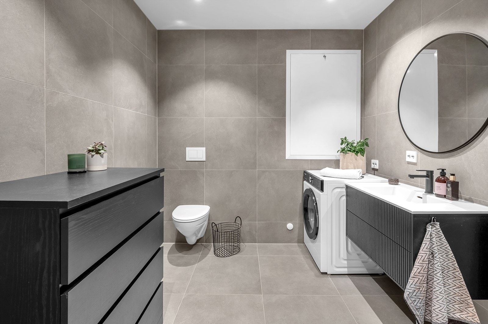 Delikat og påkostet bad med store fliser på vegger og gulv. Her er det opplegg til vaskemaskin. Galleribilde