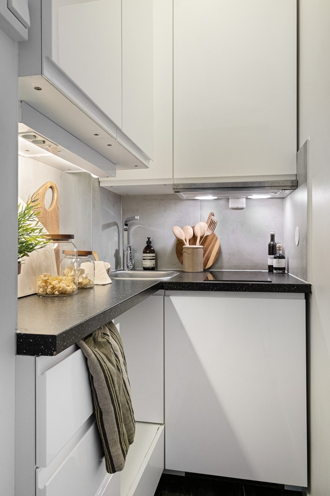 Tidsriktig glatt innredning fra IKEA (2018), soft close, fliser over benk, armatur, laminat benkeplate med nedfelt stålkum og keramisk topp, integrert kjøleskap. Det er kjøkkenventilator med kullfilter. Galleribilde