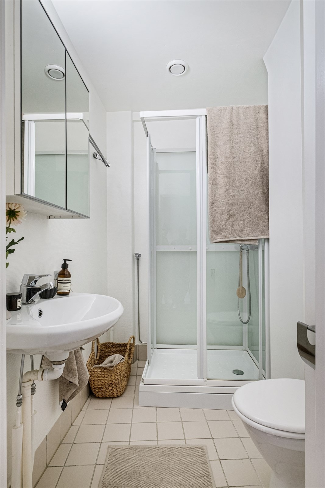 Baderom med flislagt gulv, malt strie på vegger, varmekabler, avtrekk, speilskap, armatur, opplegg for vaskemaskin, servant, dusjkabinett, toalett. Galleribilde