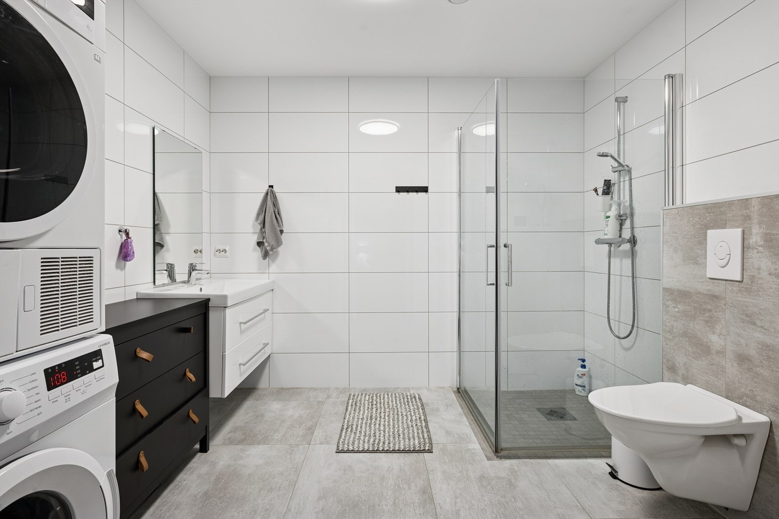 Praktikantdel: Baderommet har flislagte gulv og vegger, malte takplater, samt dusjhjørne med herdet glassdør og en praktisk baderomsinnredning med porselensvask og vegghengt toalett. Galleribilde