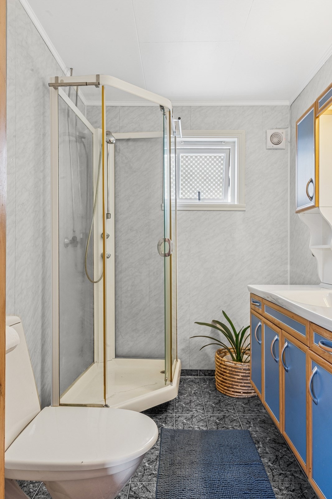 Lyst bad med flislagt gulv. Badet er utstyrt med dusjkabinett og gulvstående toalett. Galleribilde