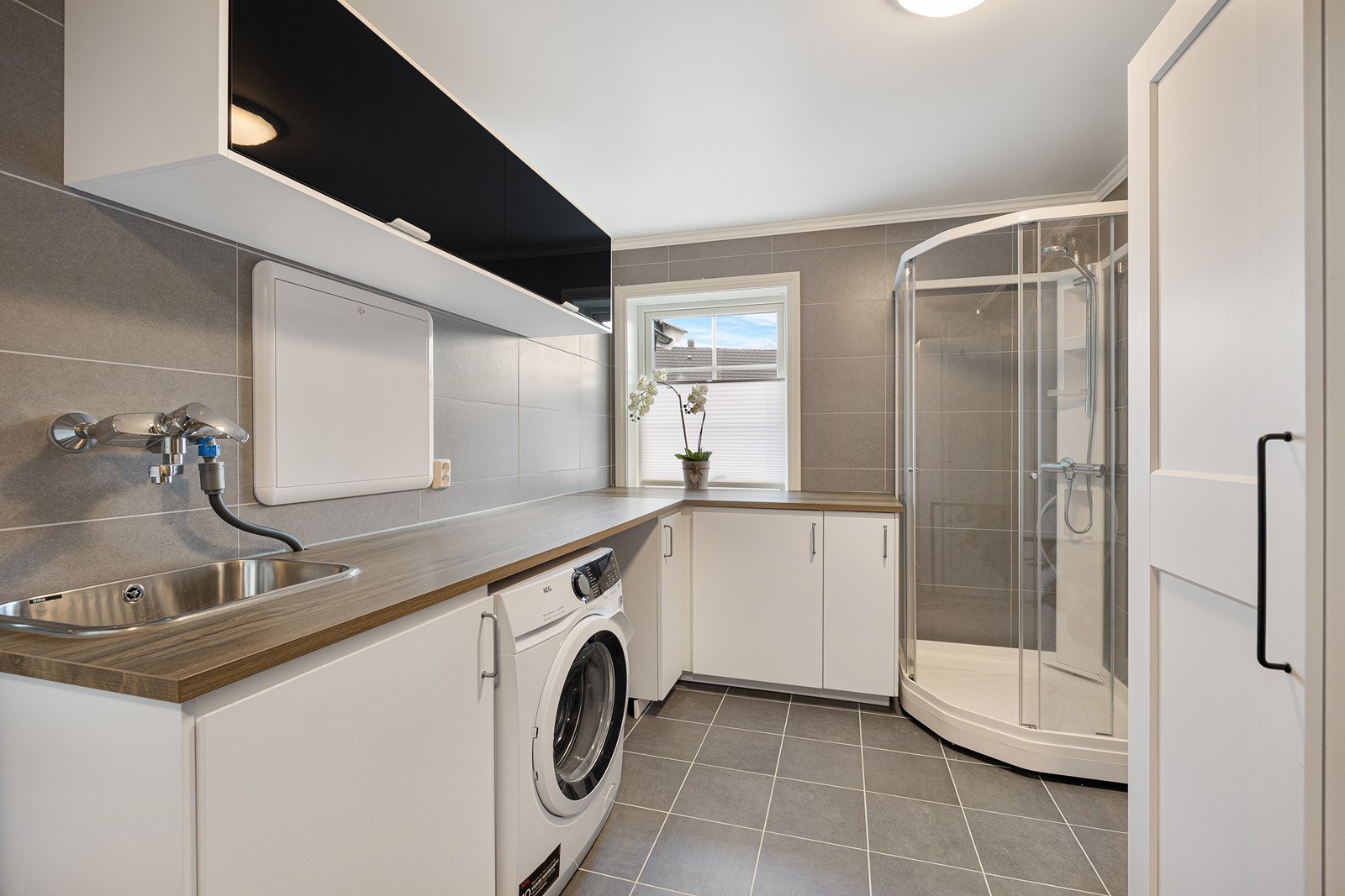 Det meste av vaskerommets innredning er plassert på den ene veggen og består av over- og benkeskap, med fronter i sort og hvitt. Innredningen har vaskekum i benk og nisje til vaskemaskin/tørketrommel. Galleribilde