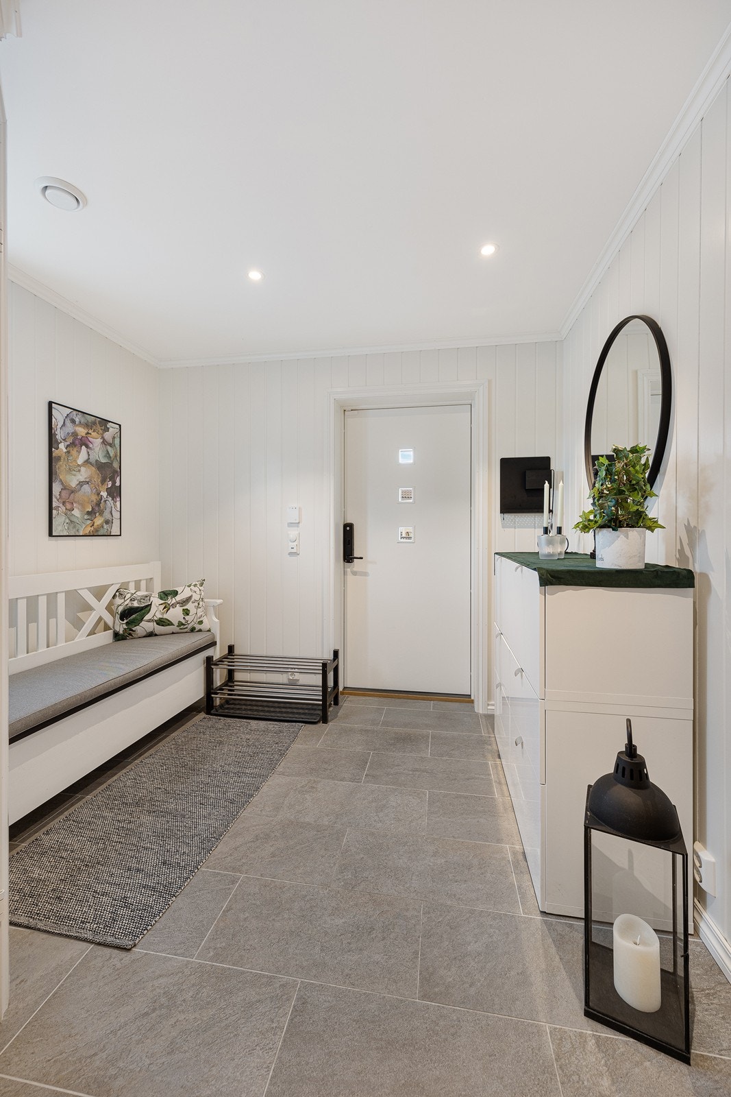 Den innbydende entreen har grå fliser på gulv og kremhvite panelvegger. Rommet har downlights i tak og det er varme i gulvet. Galleribilde
