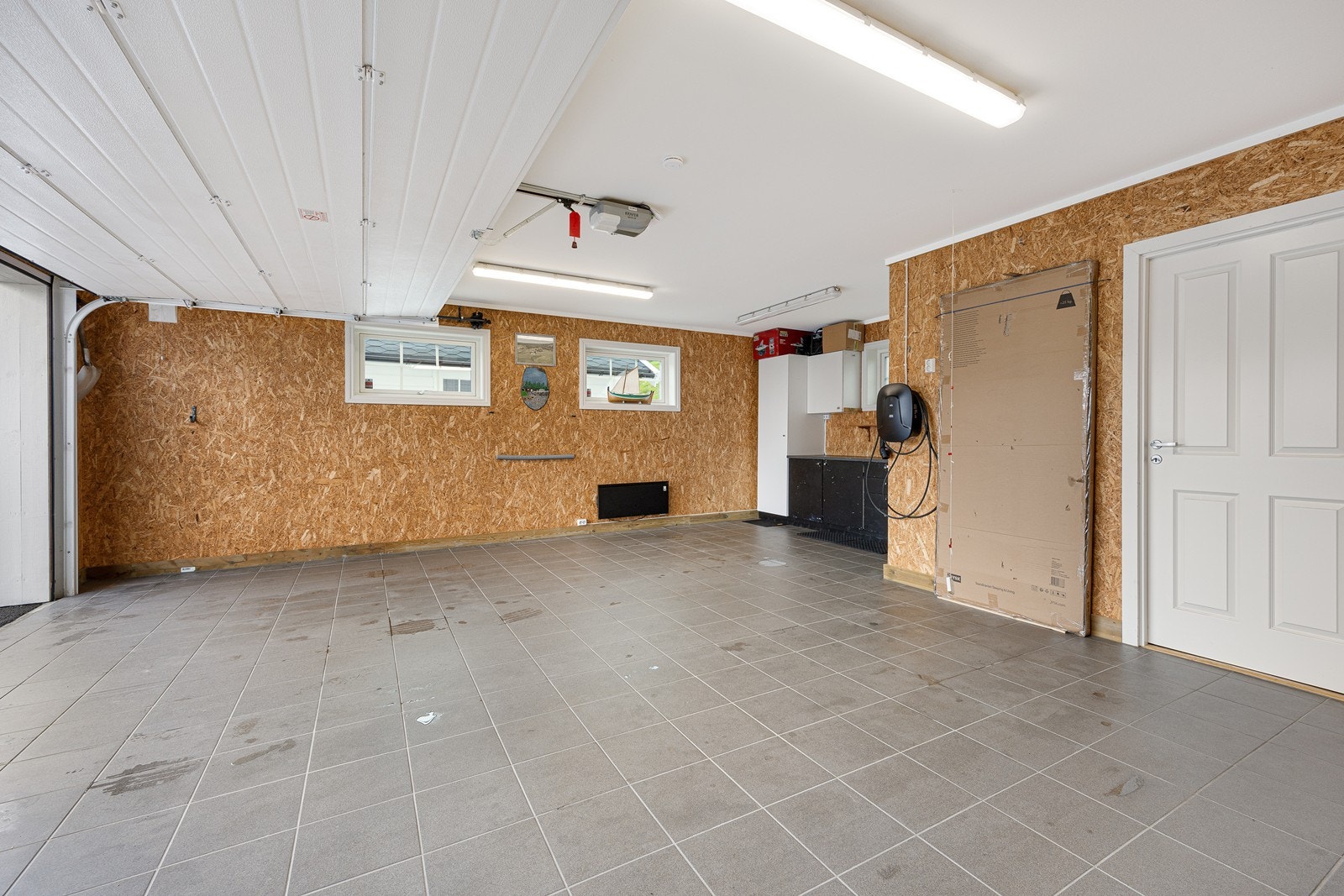 Den doble garasjen er på 50 kvm. og har flissatt gulv, skapinnredning og dør direkte til vaskerommet. Det er montert elbillader i garasjen. Galleribilde