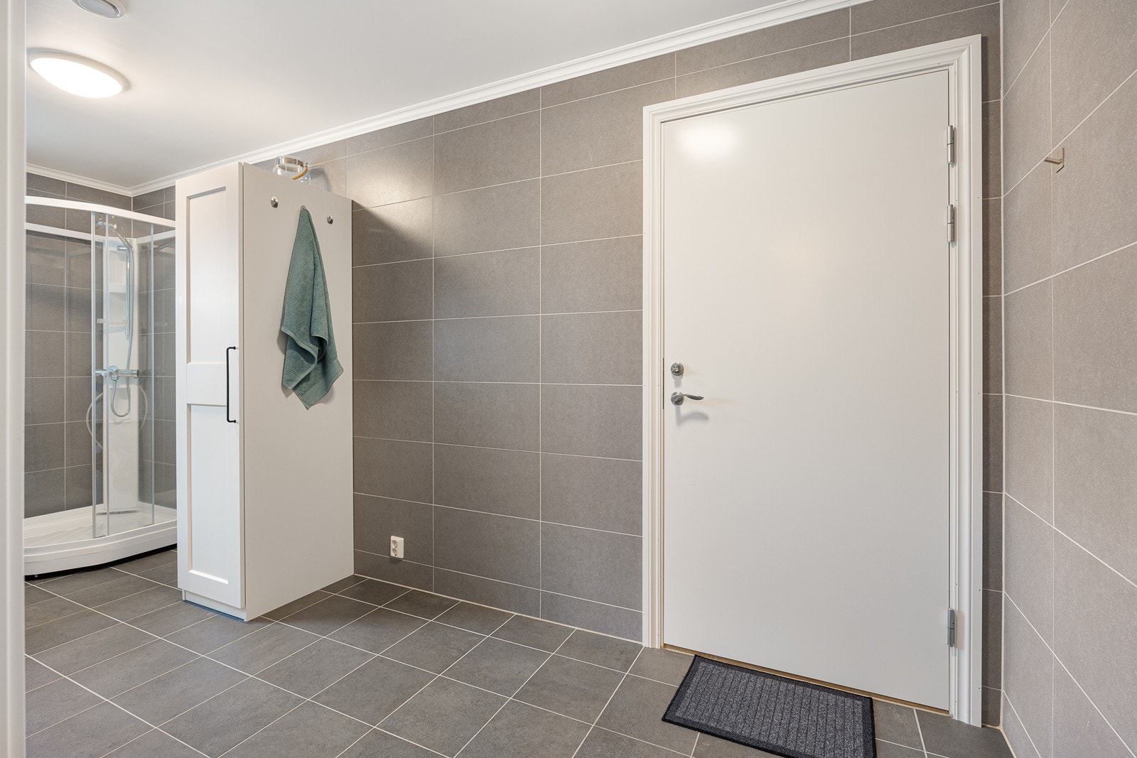 Vaskerommet har pene, like fliser på gulv og vegger, med varme i gulv, og dør til garasje. I det ene hjørnet står det et dusjkabinett. Galleribilde