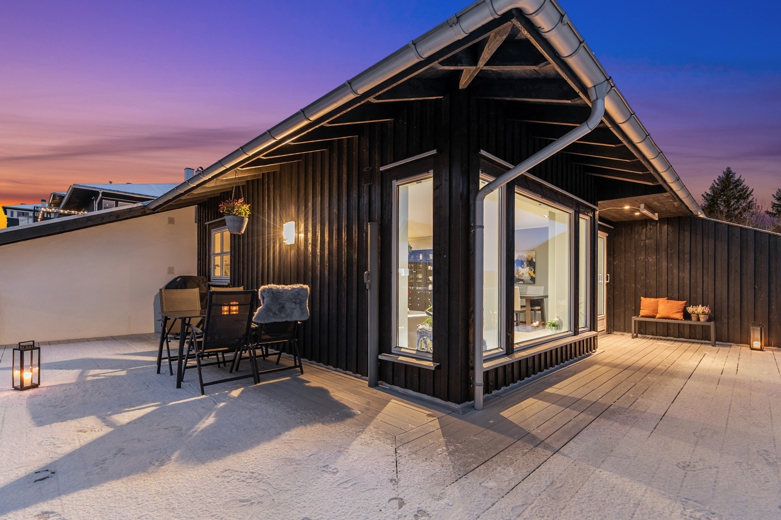 Uteplassen har terrassebord og bjelkelag i tre, rekkverk med glass og utebelysning på vegg. Galleribilde
