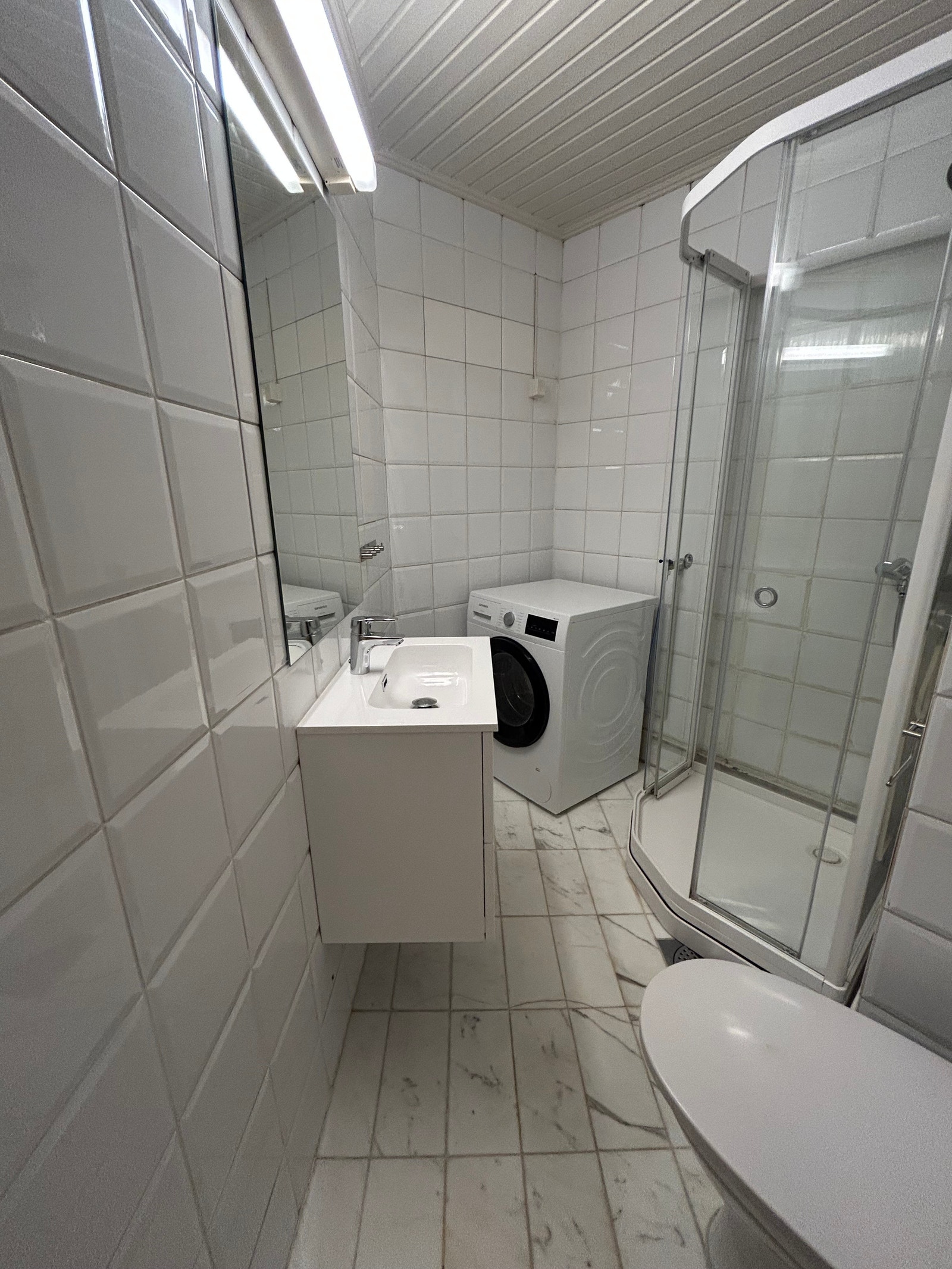 Flislagt dusjbad med varmekabler og vaskemaskin installert. Galleribilde