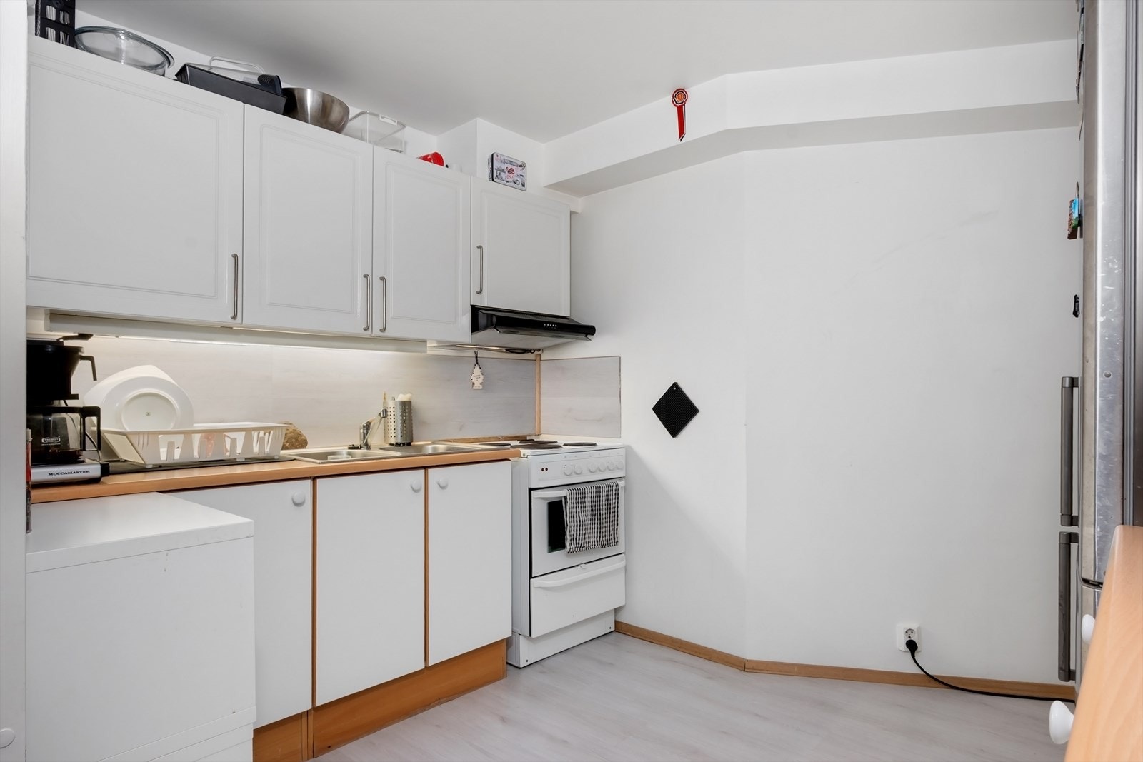 Kjøkkeninnredning fra 2007 med slette, hvite fronter og laminat benkeplate. Over- og underskap gir greit med oppbevaringsplass. Galleribilde