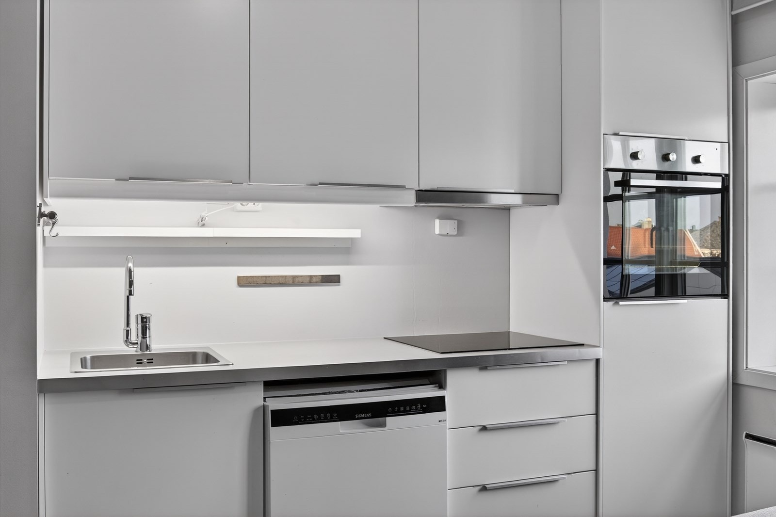 Kjøkkeninnredning med hvite slette fronter, benkeplate i laminat og integrerte hvitevarer. Galleribilde