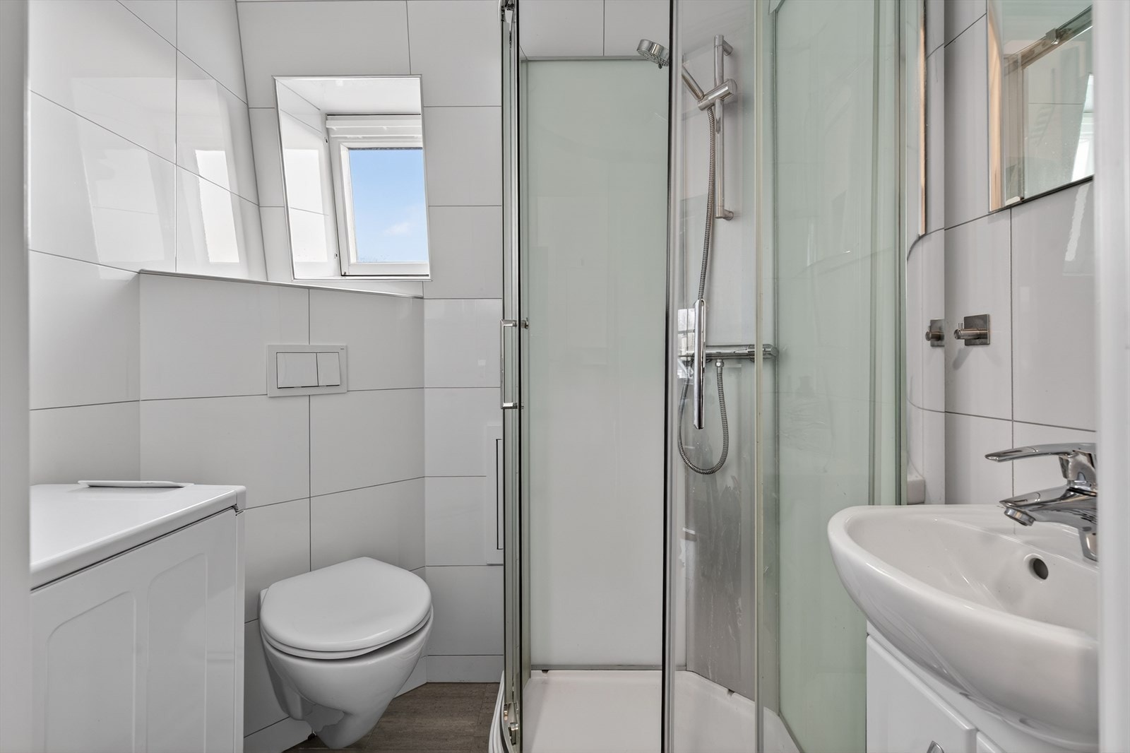 Helfliset bad som inneholder dusjkabinett, seksjon med servant, vegghengt toalett og opplegg for vaskemaskin. Galleribilde