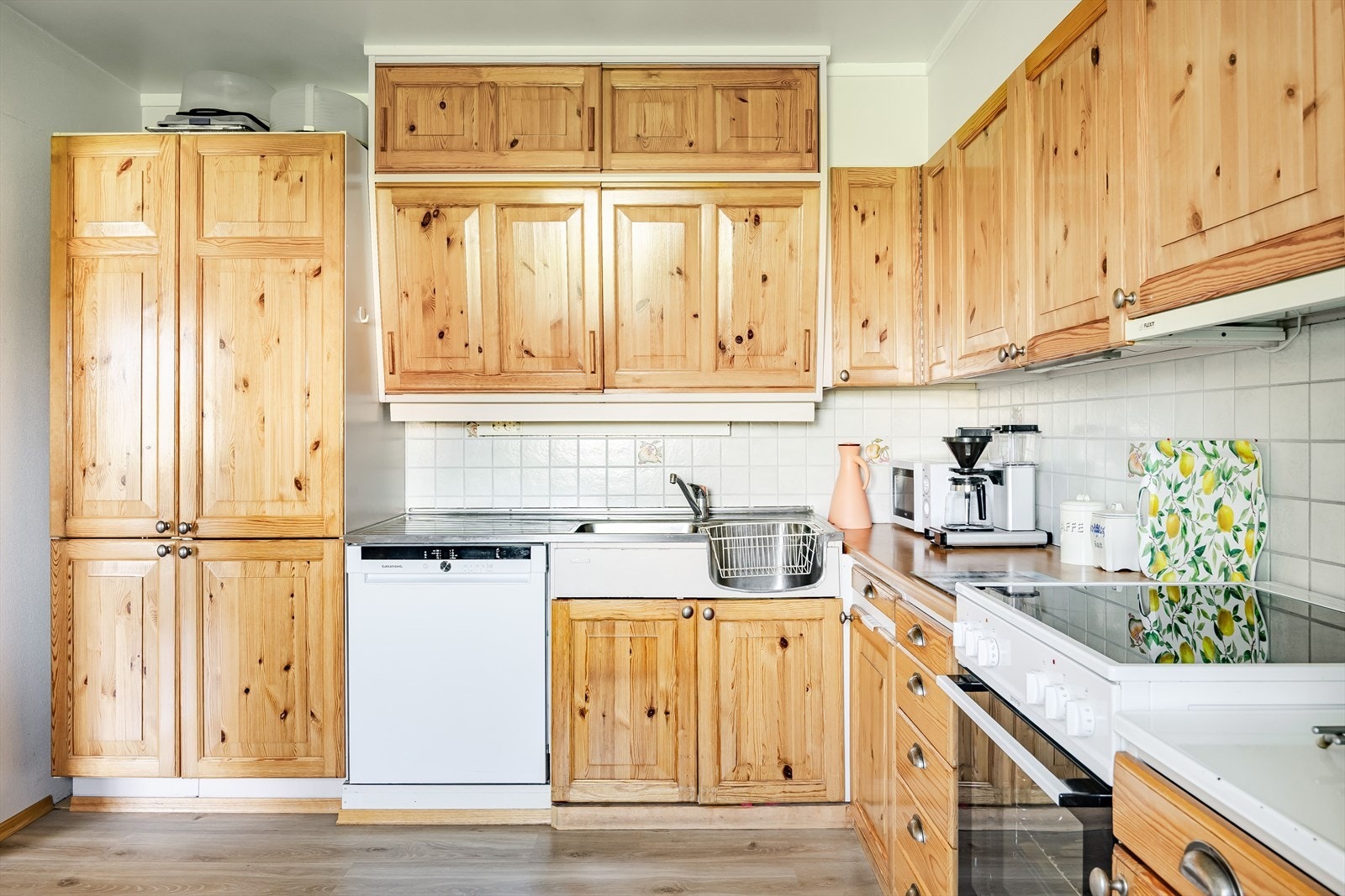 Kjøkkeninnredningen har profilerte heltre fronter, laminerte benkeplater, benkebeslag med nedfelt oppvaskkum og fliser i benkeryggen. Fronter fremstår som nyere enn skrogene. Galleribilde