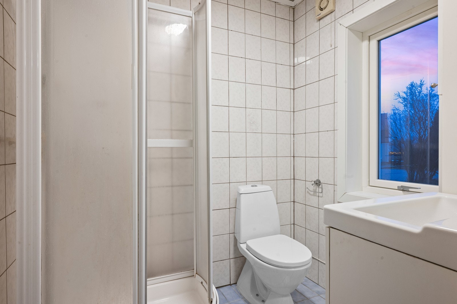 Flislagt bad utstyrt med toalett, servant og dusjkabinett. Galleribilde