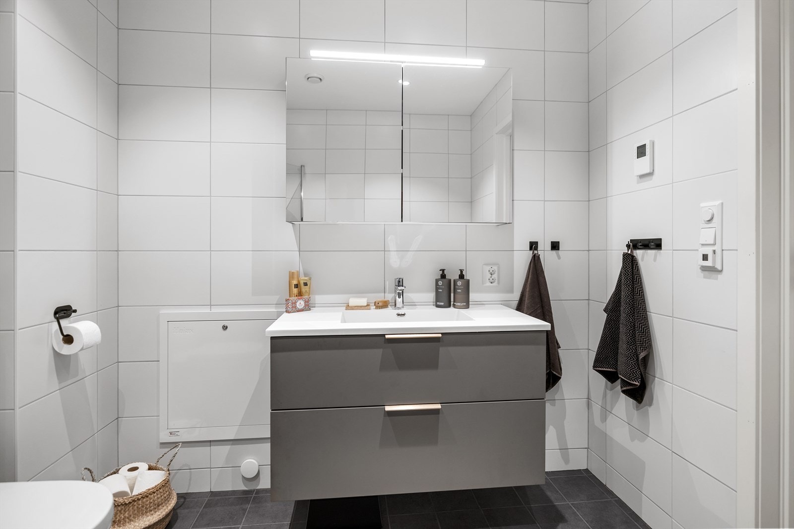 Badet fremstår som moderne og tidløst, utstyrt med innredning med nedfelt servant, veggmontert toalett og dusjhjørne med glassvegger. Galleribilde